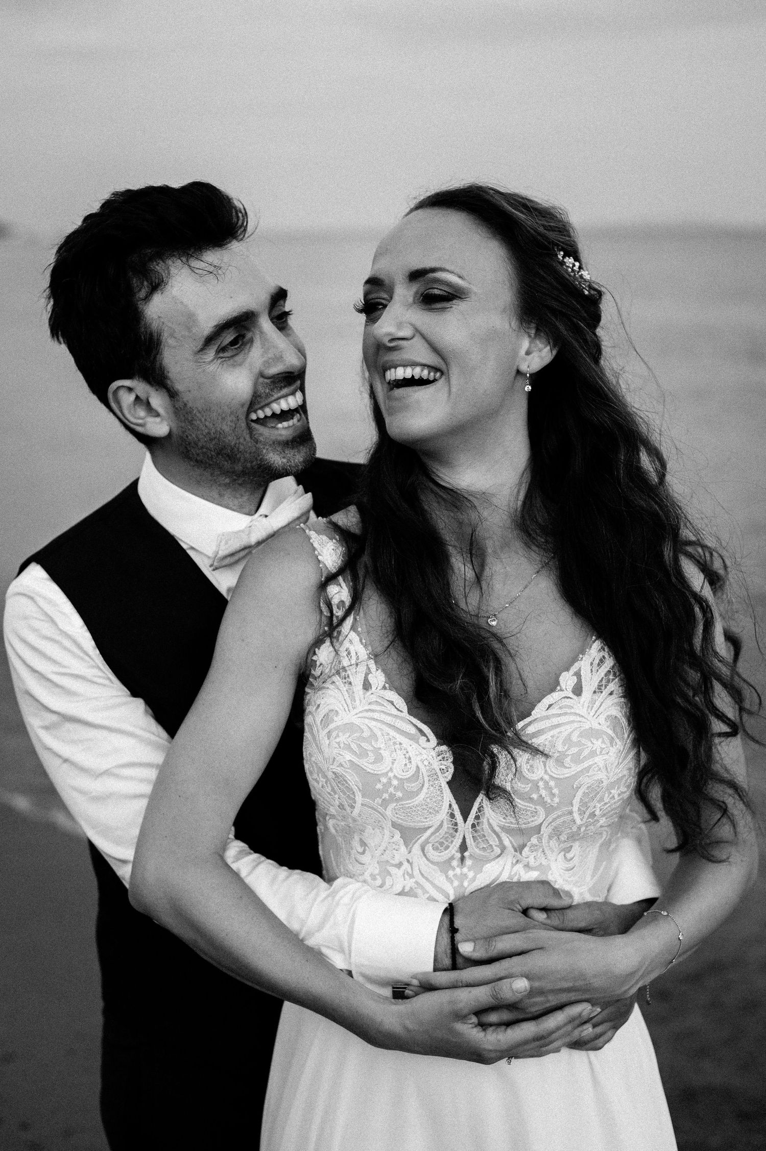 Intimate black and white portrait of newlyweds sharing laughter by the sea.