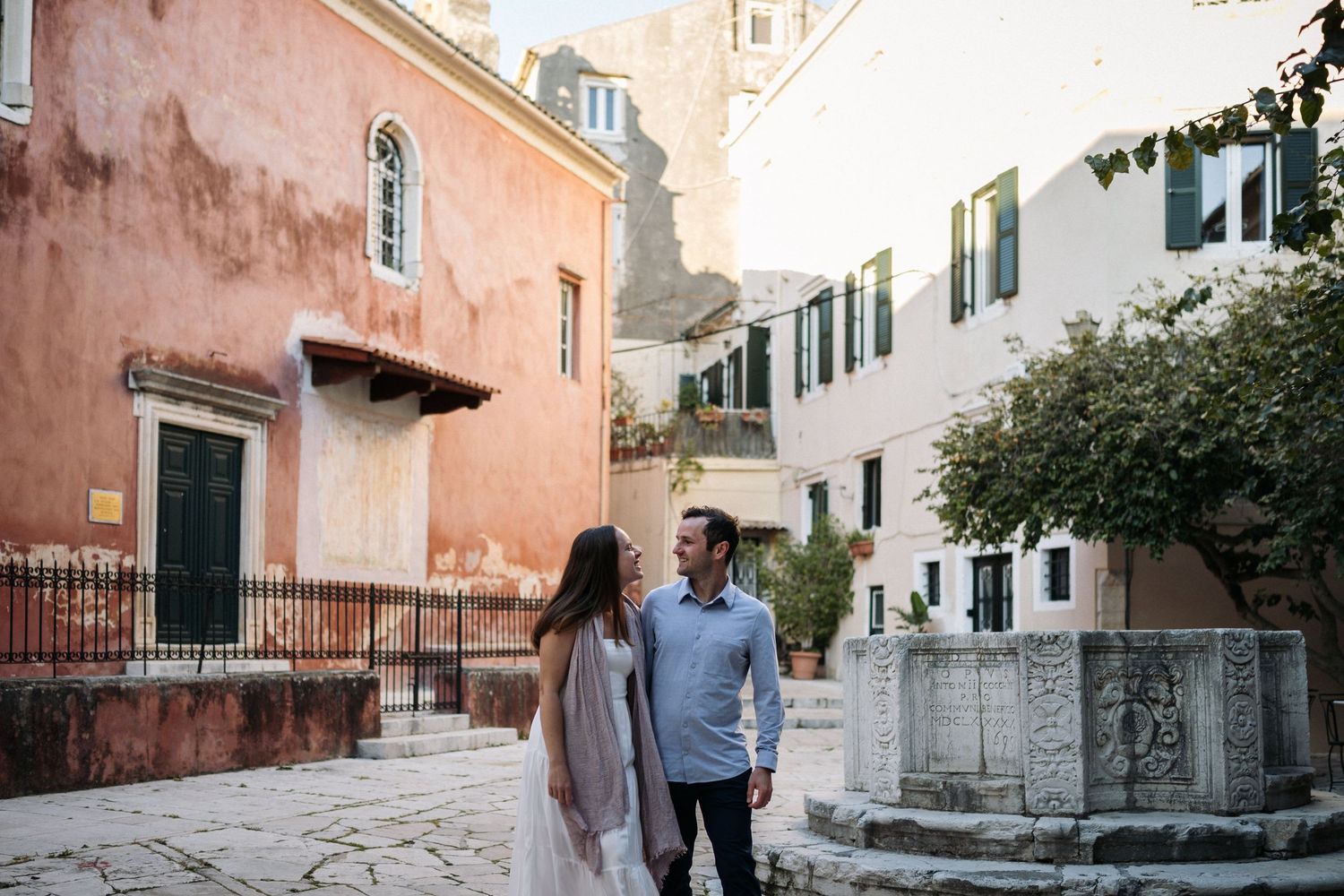 Couple strolling along a pink-walled Mediterranean street with traditional architecture.