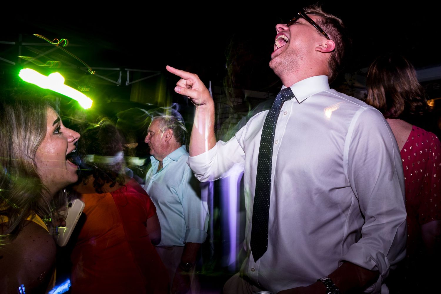 Energetic dancing and celebrating under green lighting at a nighttime party venue.