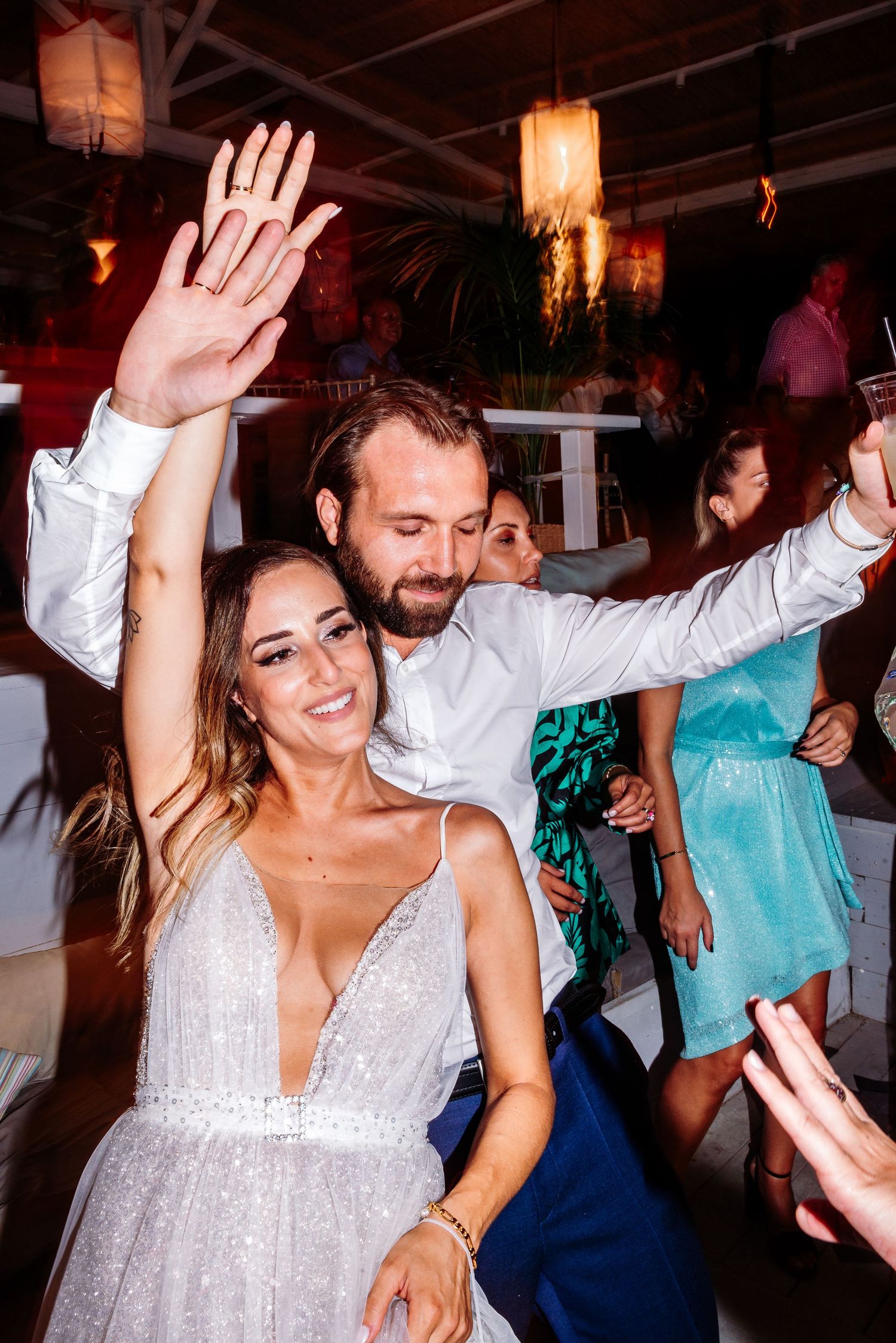 Joyful celebration with guests dancing and raising hands during wedding reception.
