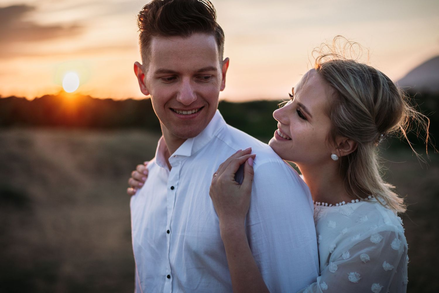Intimate sunset portrait of a couple sharing a tender moment in a field.