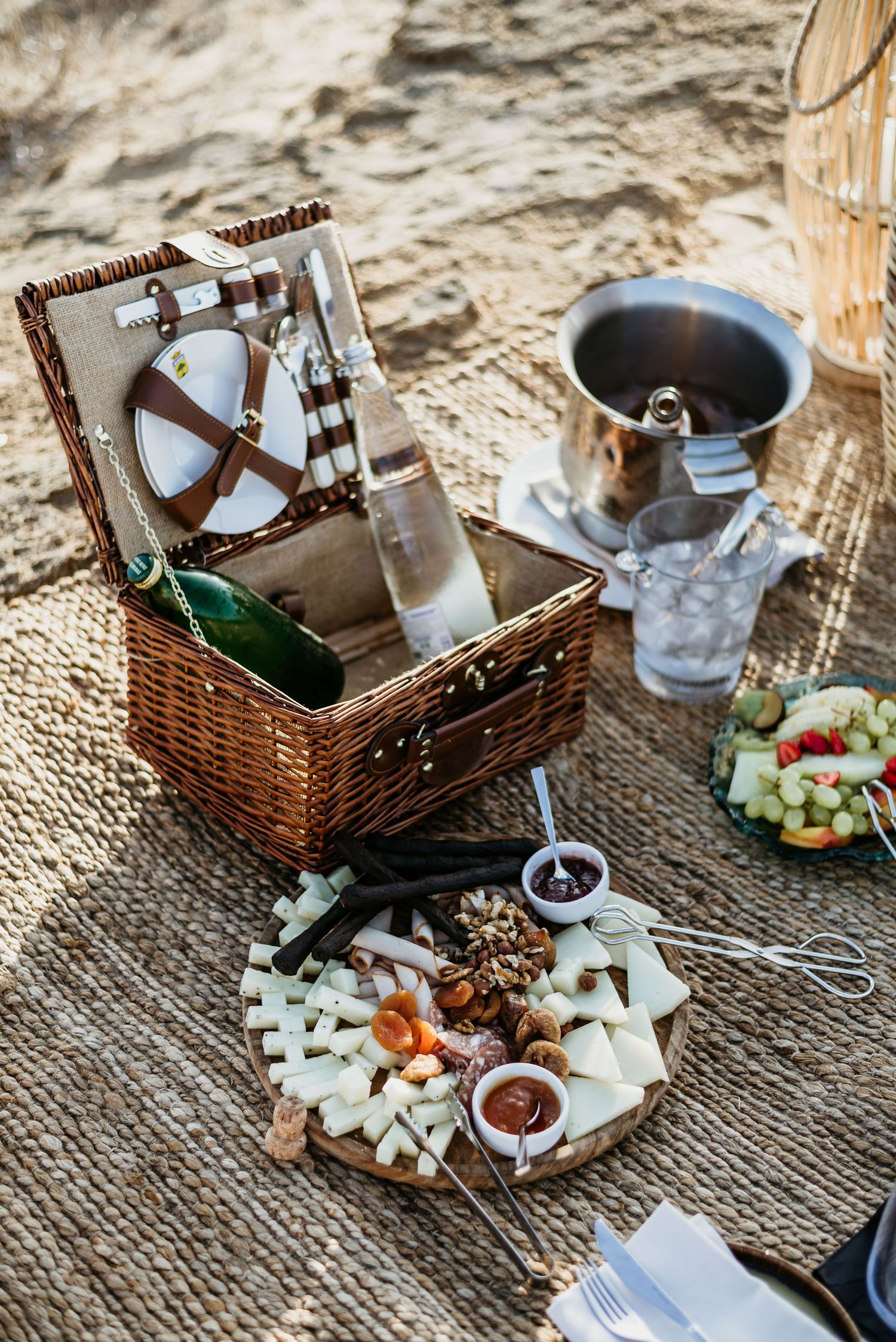 Elegant picnic spread with wicker basket, cheese board, and wine accessories on textured blanket.