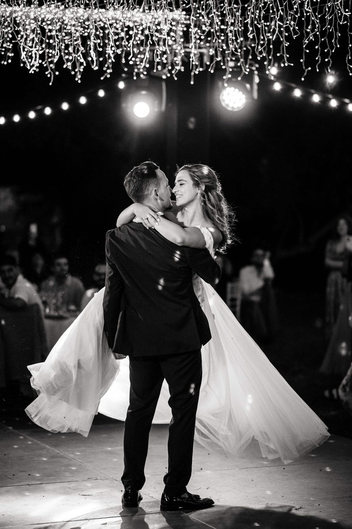 Couple performs romantic dip dance move under twinkling lights at wedding reception.