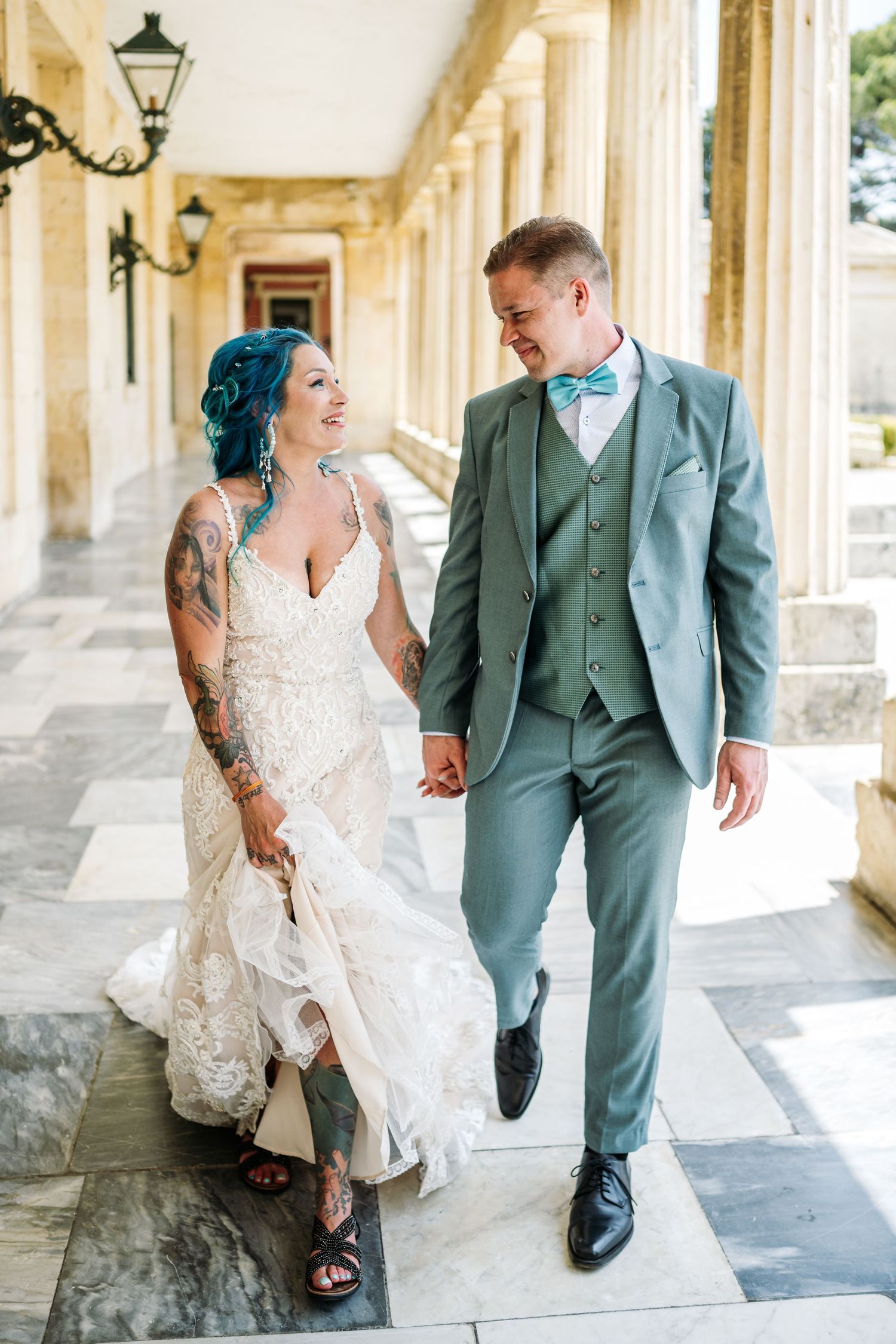Wedding couple walking and laughing together under elegant stone archways.