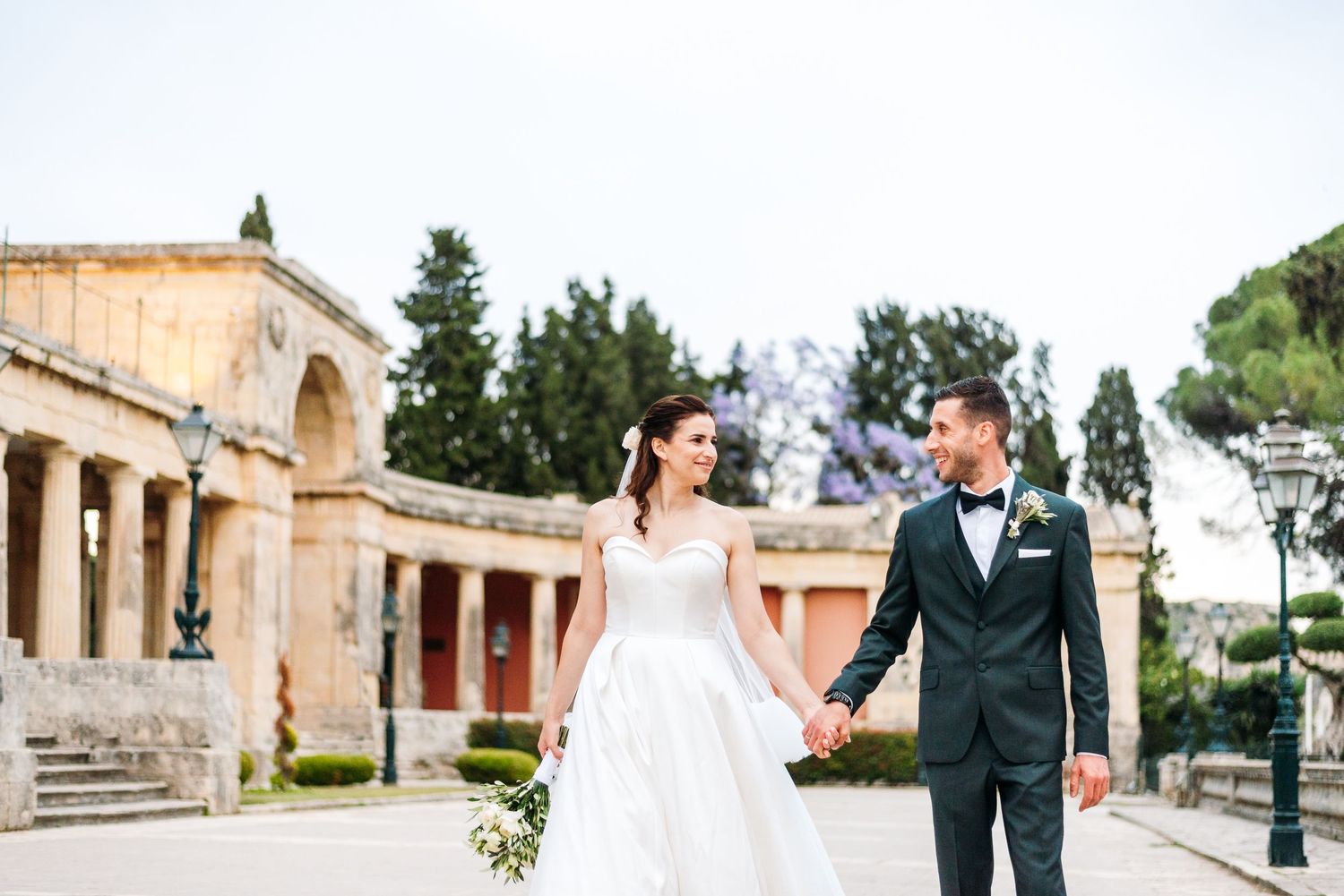 Elegant wedding couple shares romantic moments in front of Mediterranean architecture and gardens.