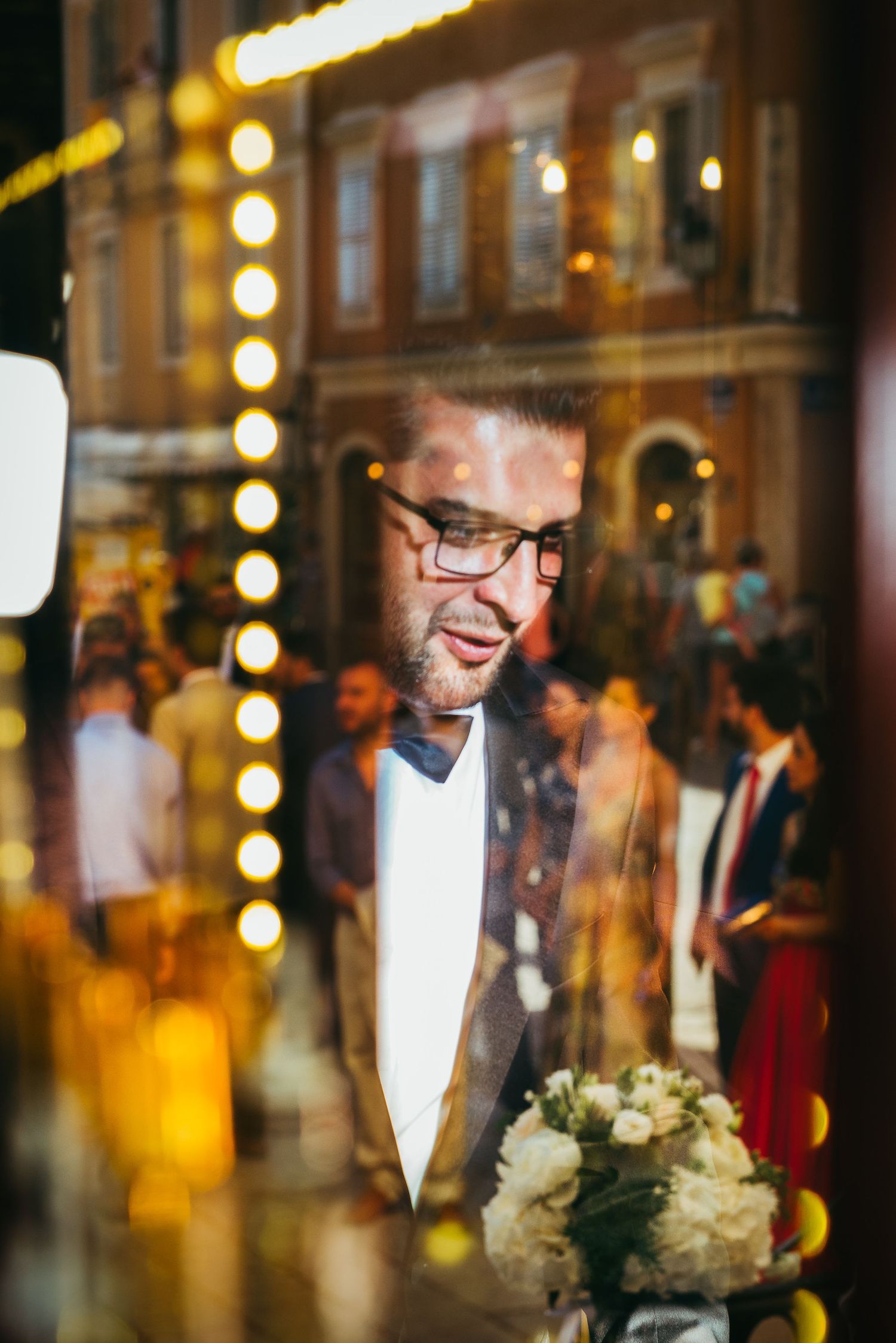 Wedding reception scene through window glass with warm lighting and reflections.