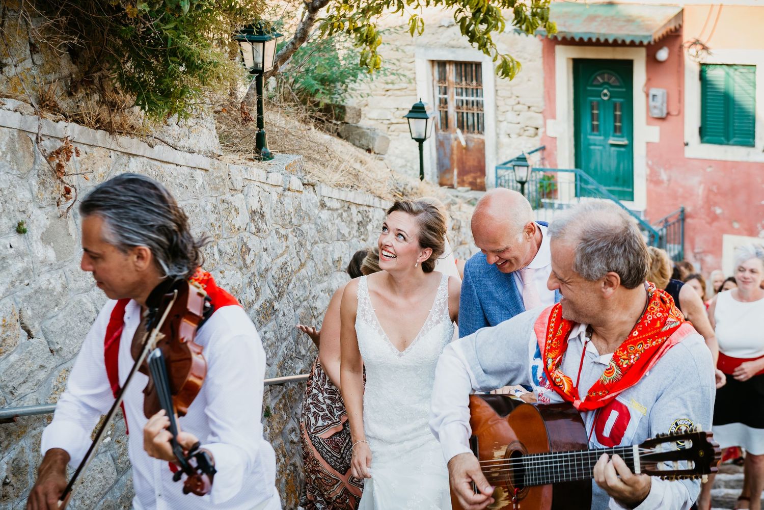 Street musicians performing with guitars and accordion in a Mediterranean village setting.
