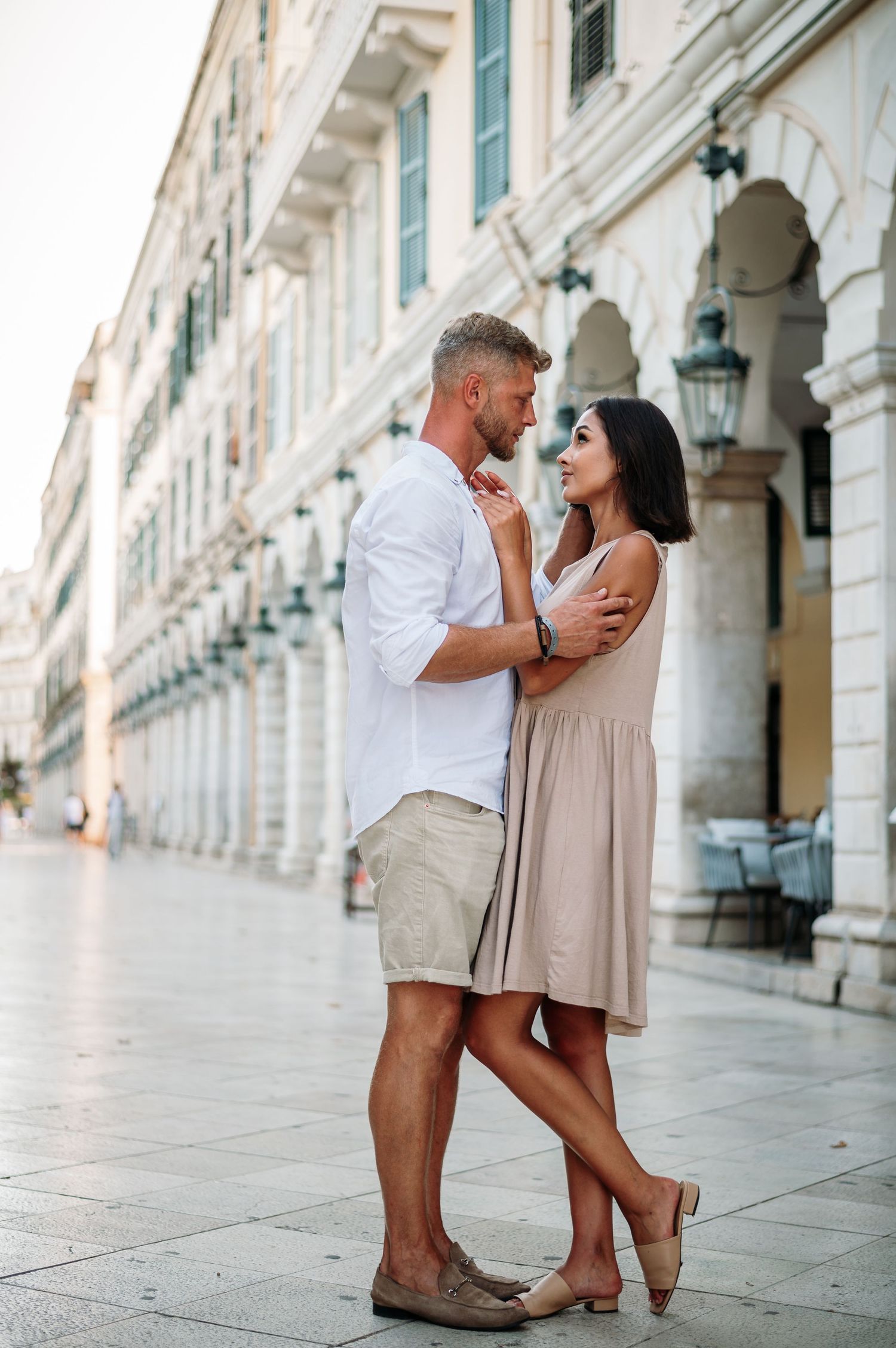 Romantic couple embracing in front of elegant white stone colonnade in European city street.