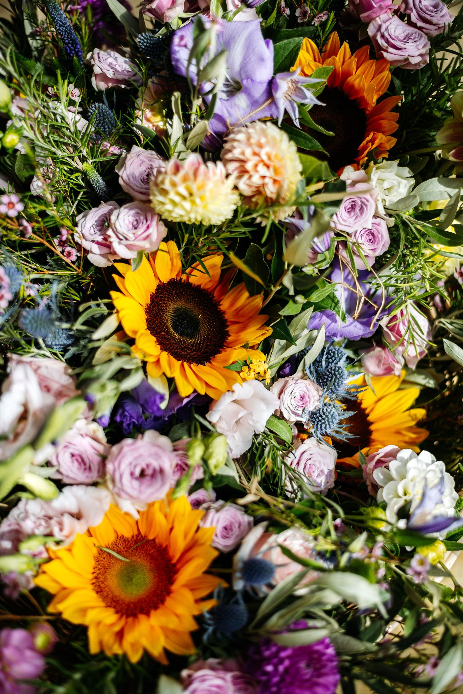 Vibrant wedding bouquet featuring sunflowers, purple roses, and mixed seasonal flowers.