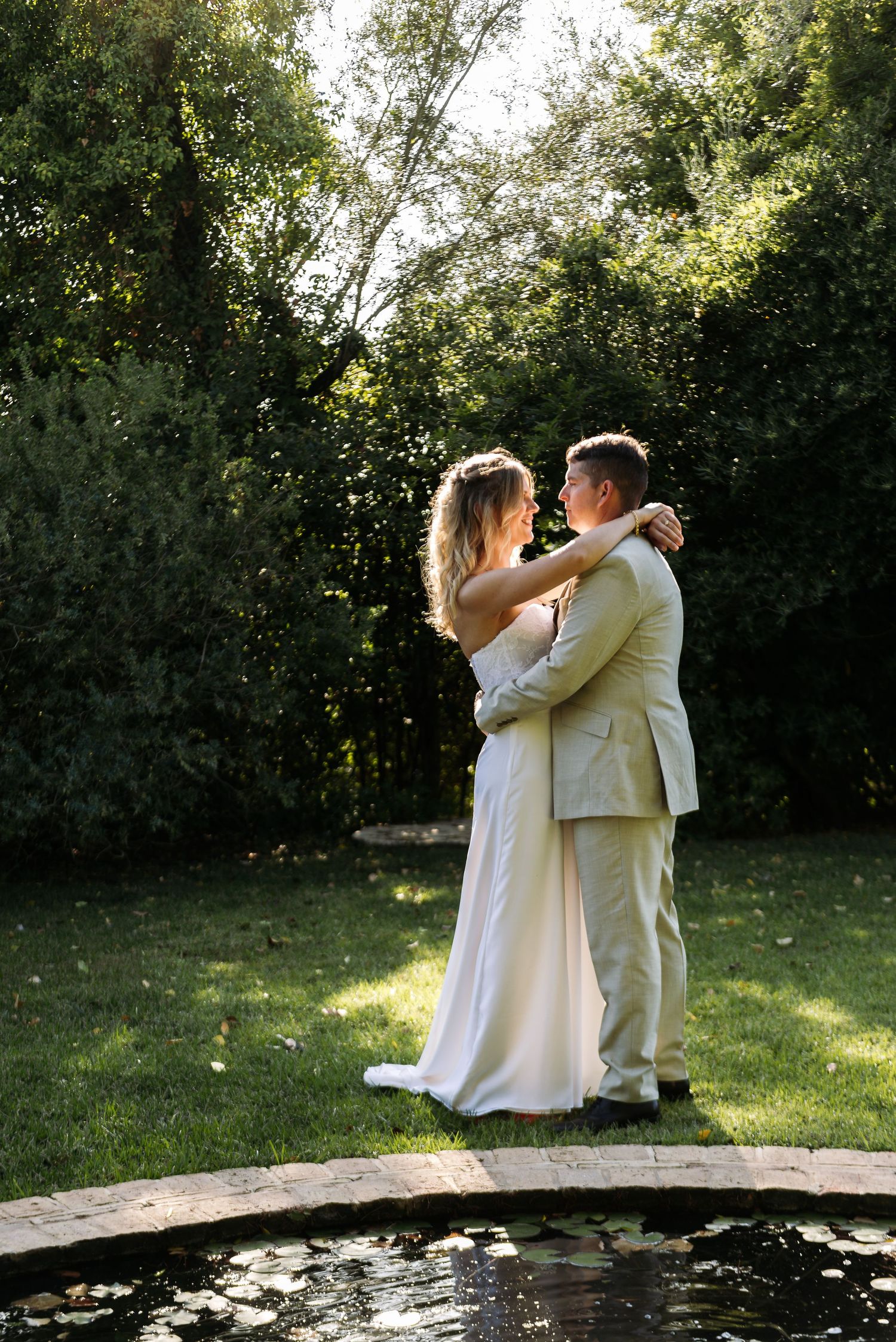 A couple shares an intimate dance moment beside a garden pond.