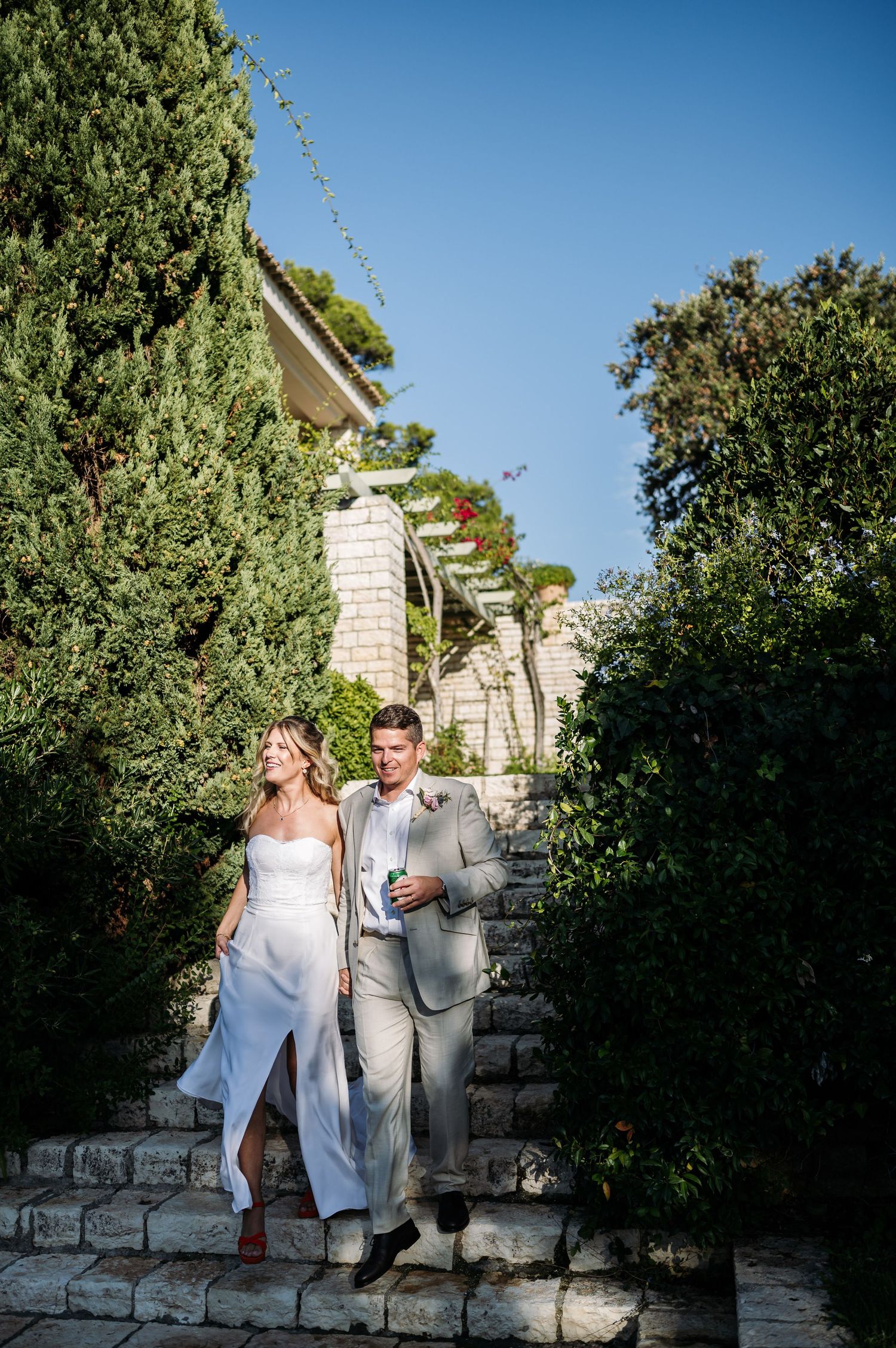Elegant couple posing on stone steps against lush garden backdrop.