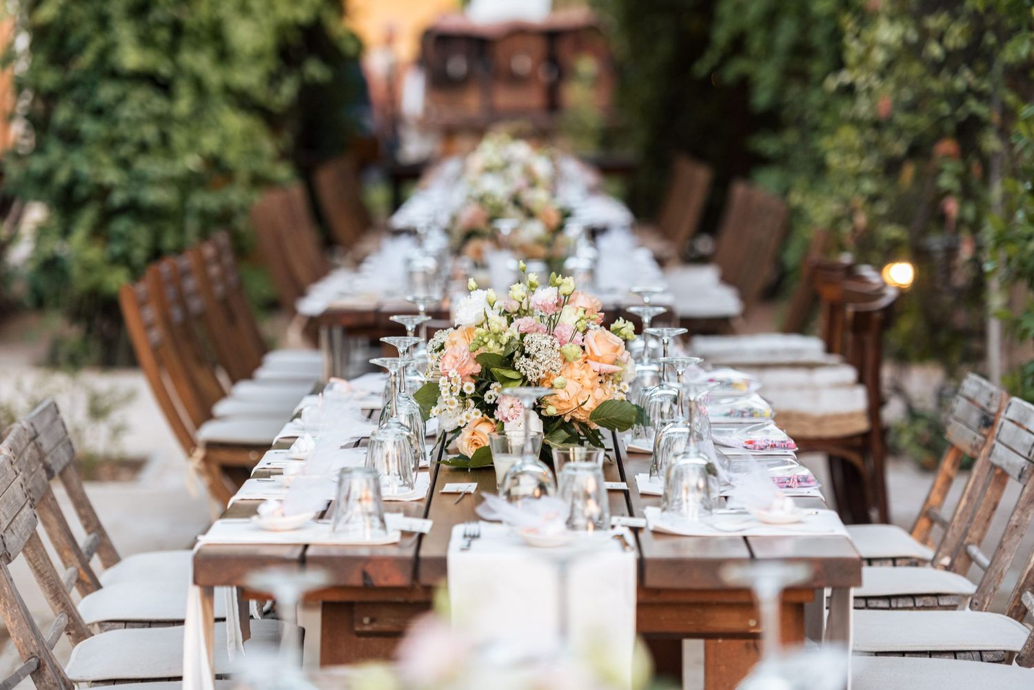 Elegant outdoor wedding reception table with white linens and floral centerpieces in a garden setting.