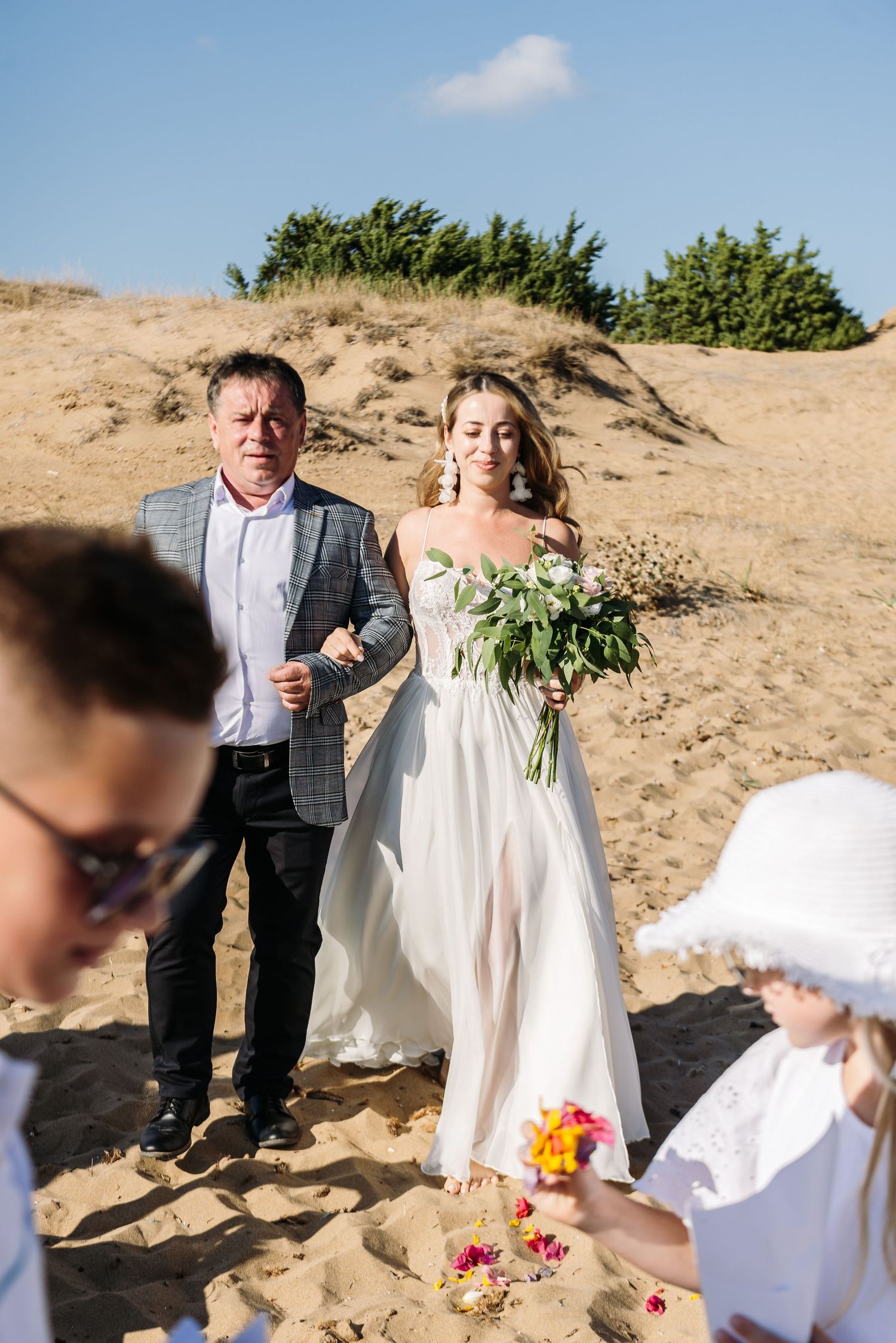 Wedding celebration on sandy beach with guests gathering around the newlyweds.