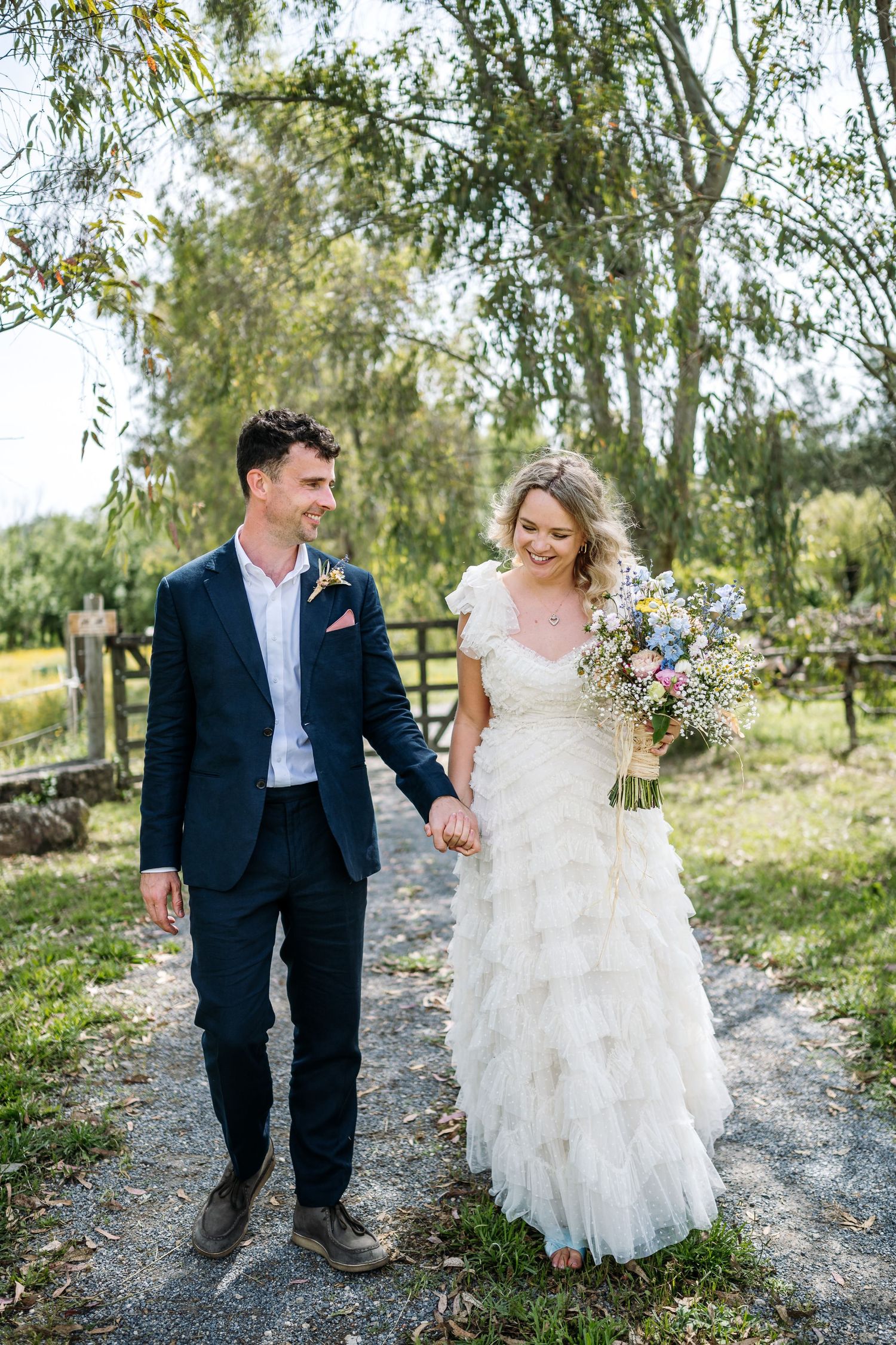 A couple walks together on a gravel path under willow trees.