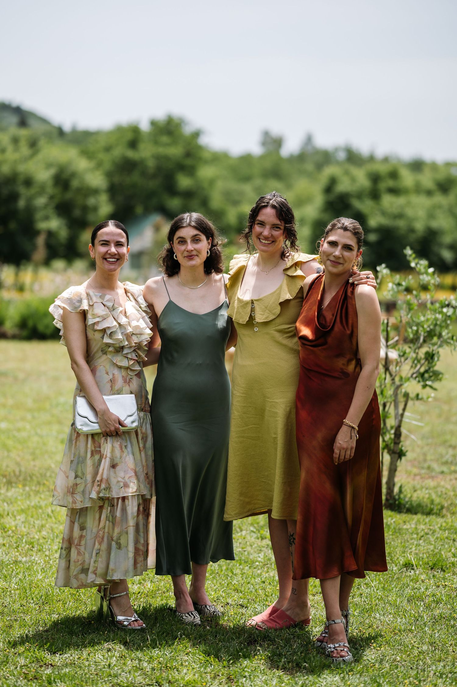 Friends in colorful dresses stand together in a sunny meadow.