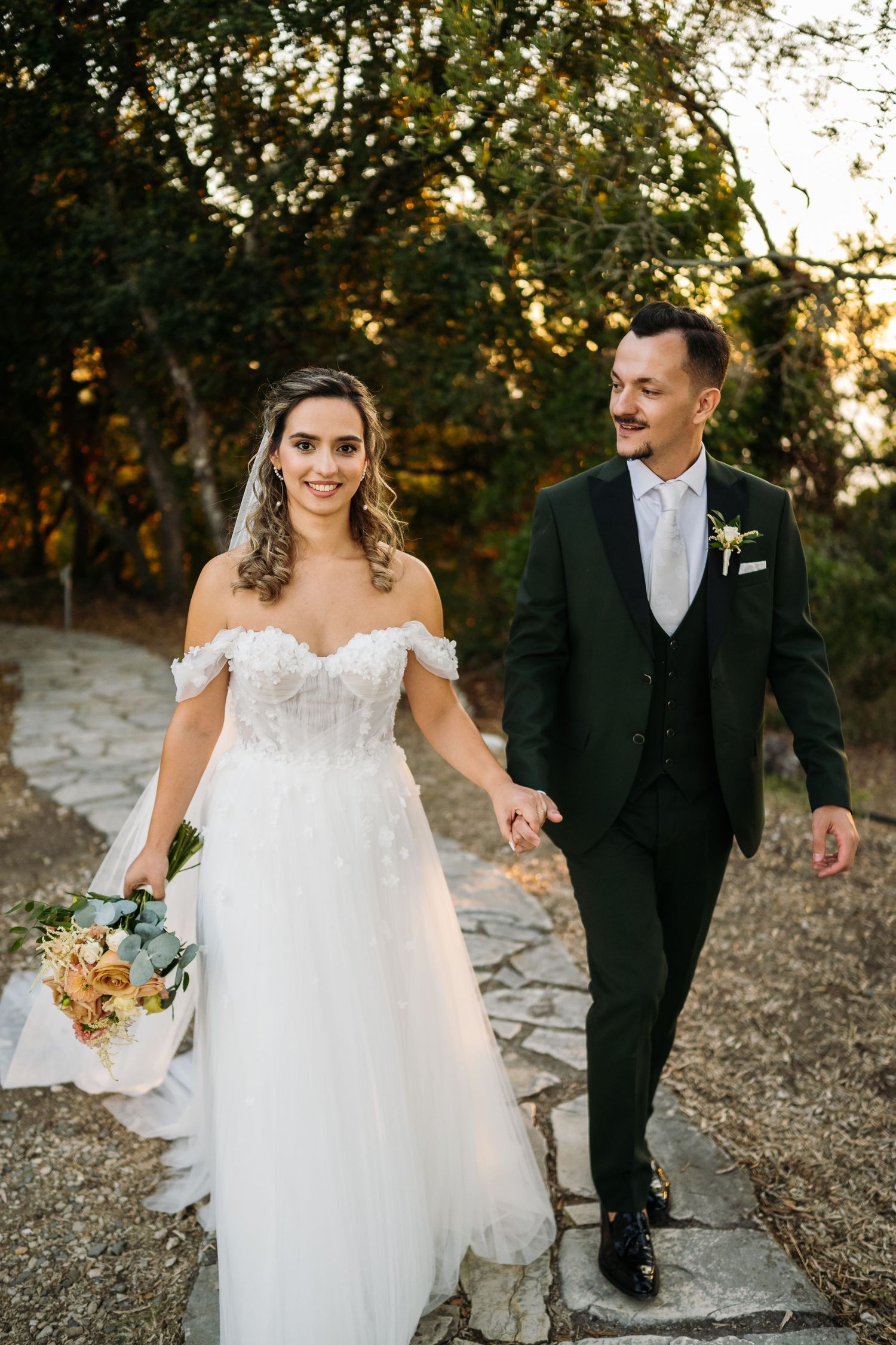 Newlywed couple walking together on a stone path during golden hour at an outdoor wedding.