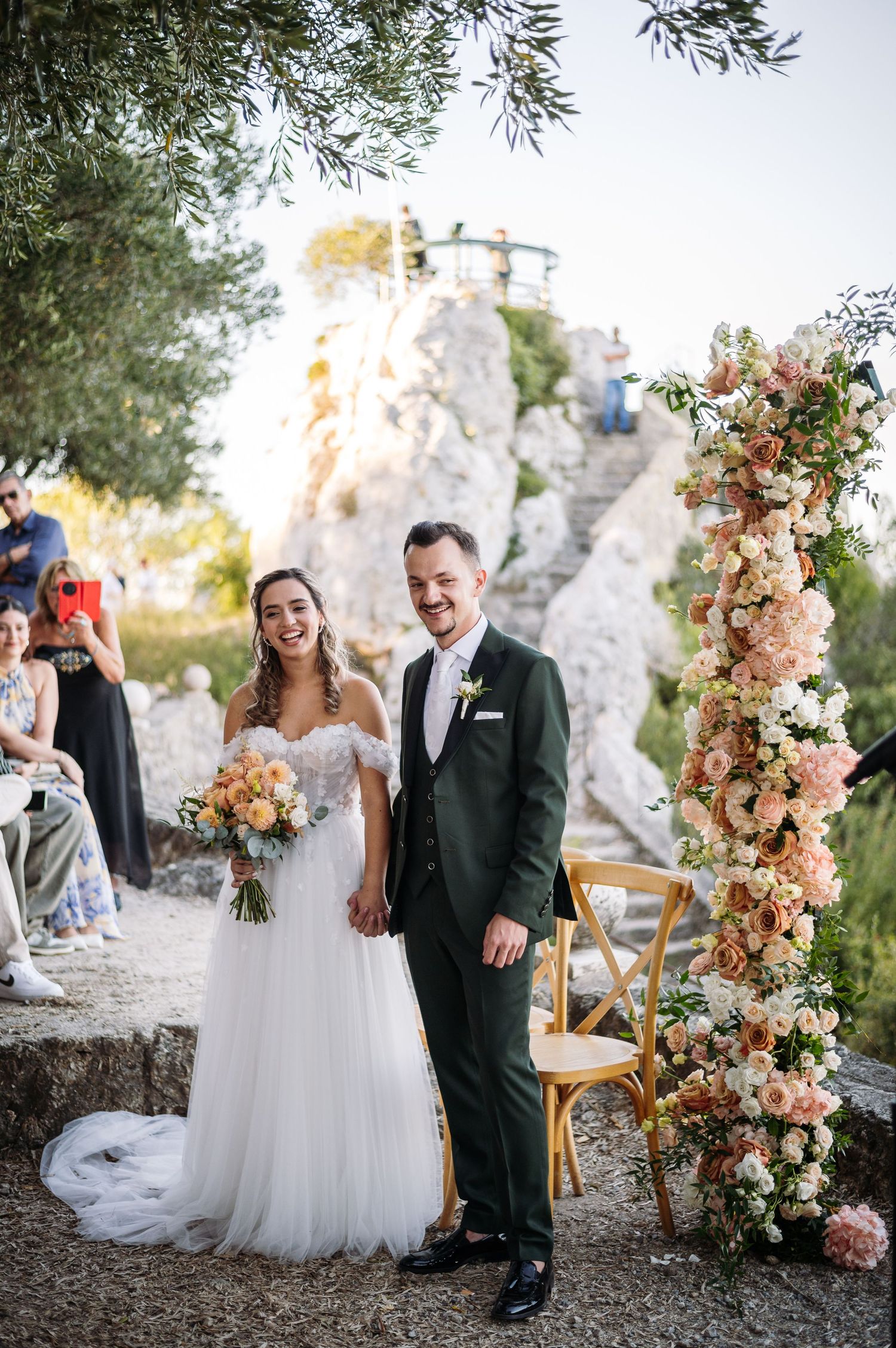 Wedding ceremony setup with peach floral arch arrangements against a dramatic cliff backdrop.