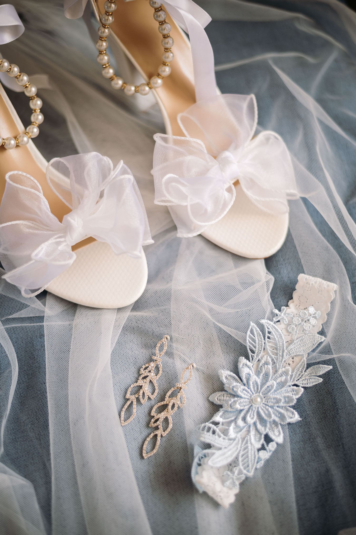 Elegant bridal accessories including white heels, pearl jewelry, and delicate lace details on tulle fabric.