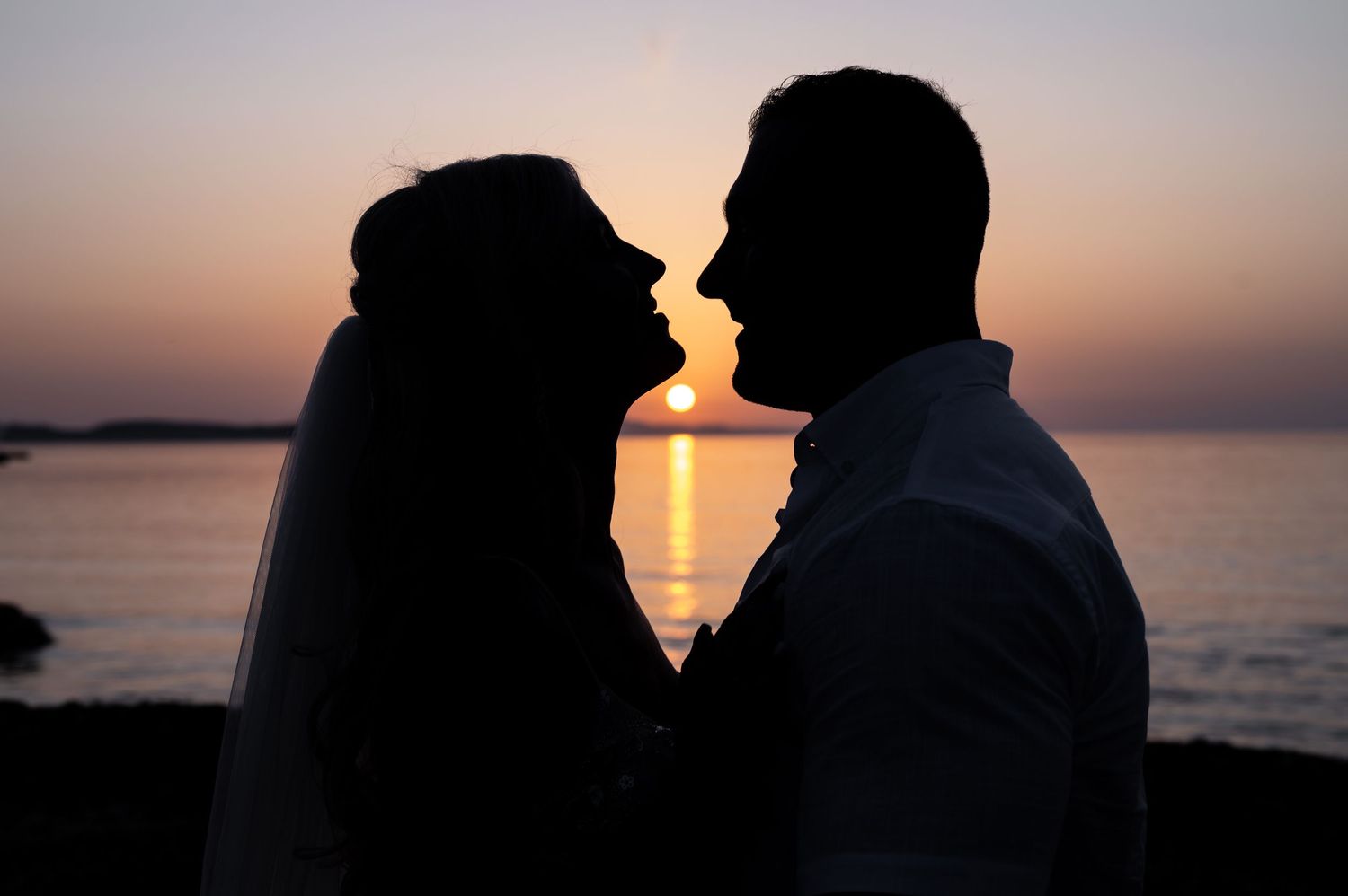 Silhouettes of a couple against a dramatic ocean sunset backdrop.