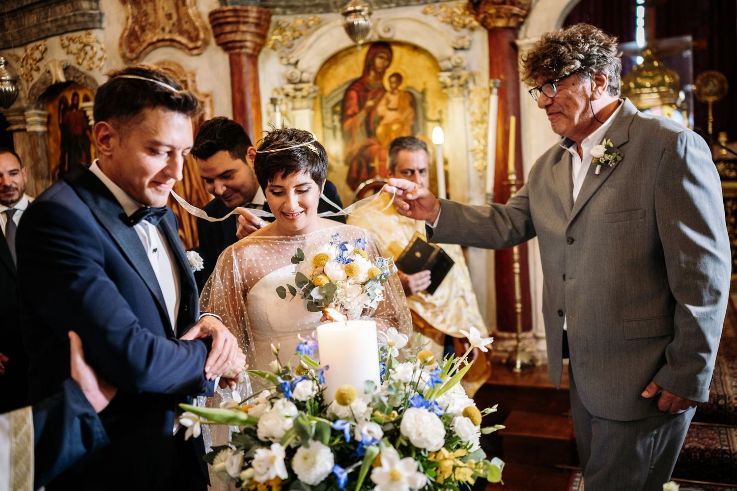 Traditional church wedding ceremony with ornate Byzantine-style religious artwork in background.