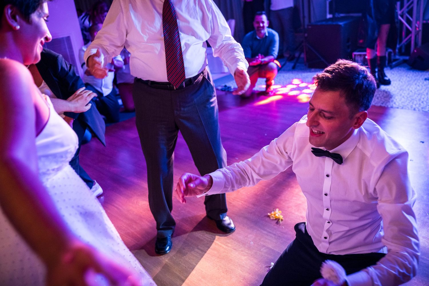 Wedding party dances under vibrant purple lighting during an energetic reception.