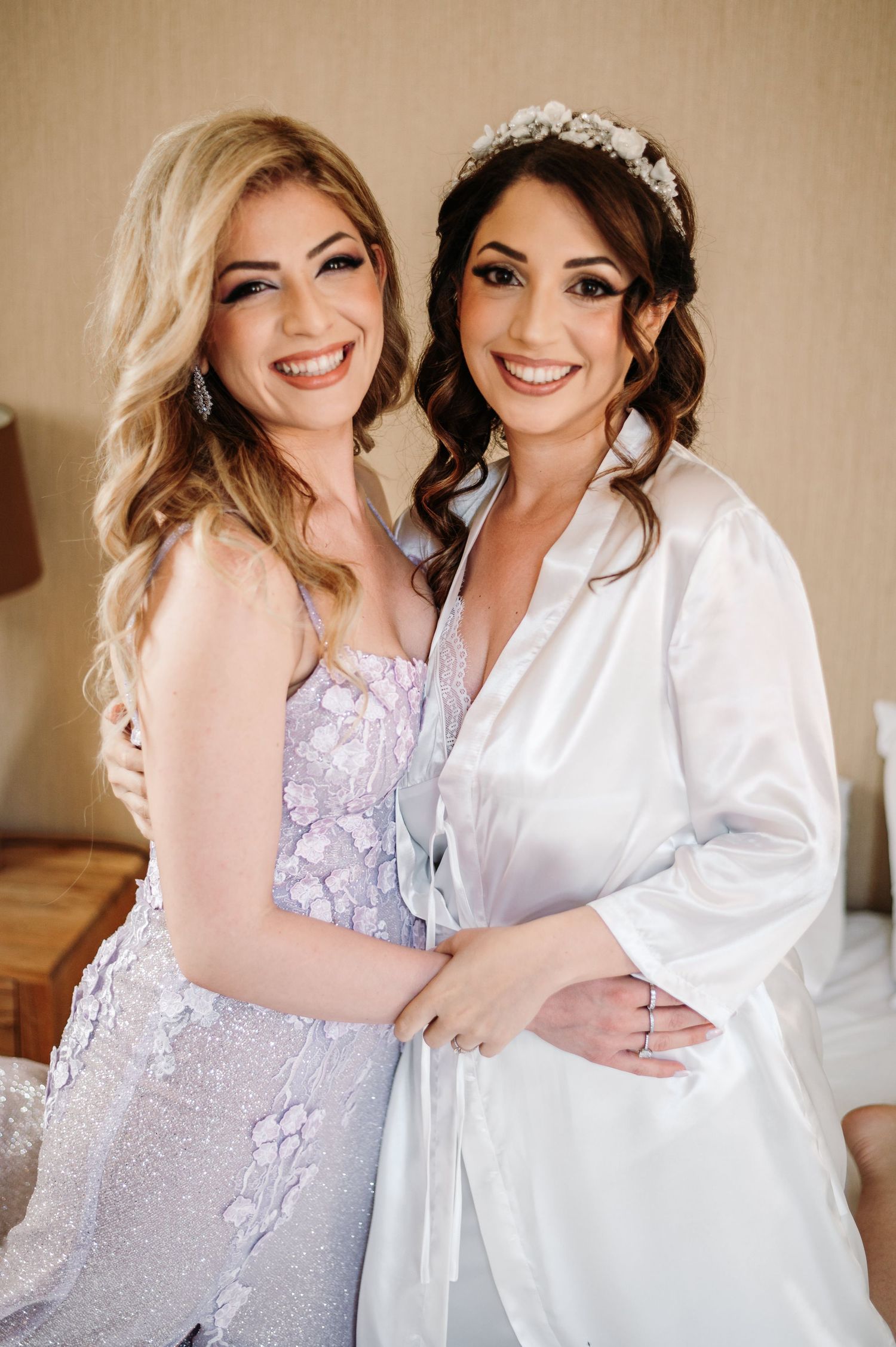 Two people in white and lavender dresses sharing joyful moments during wedding preparations.