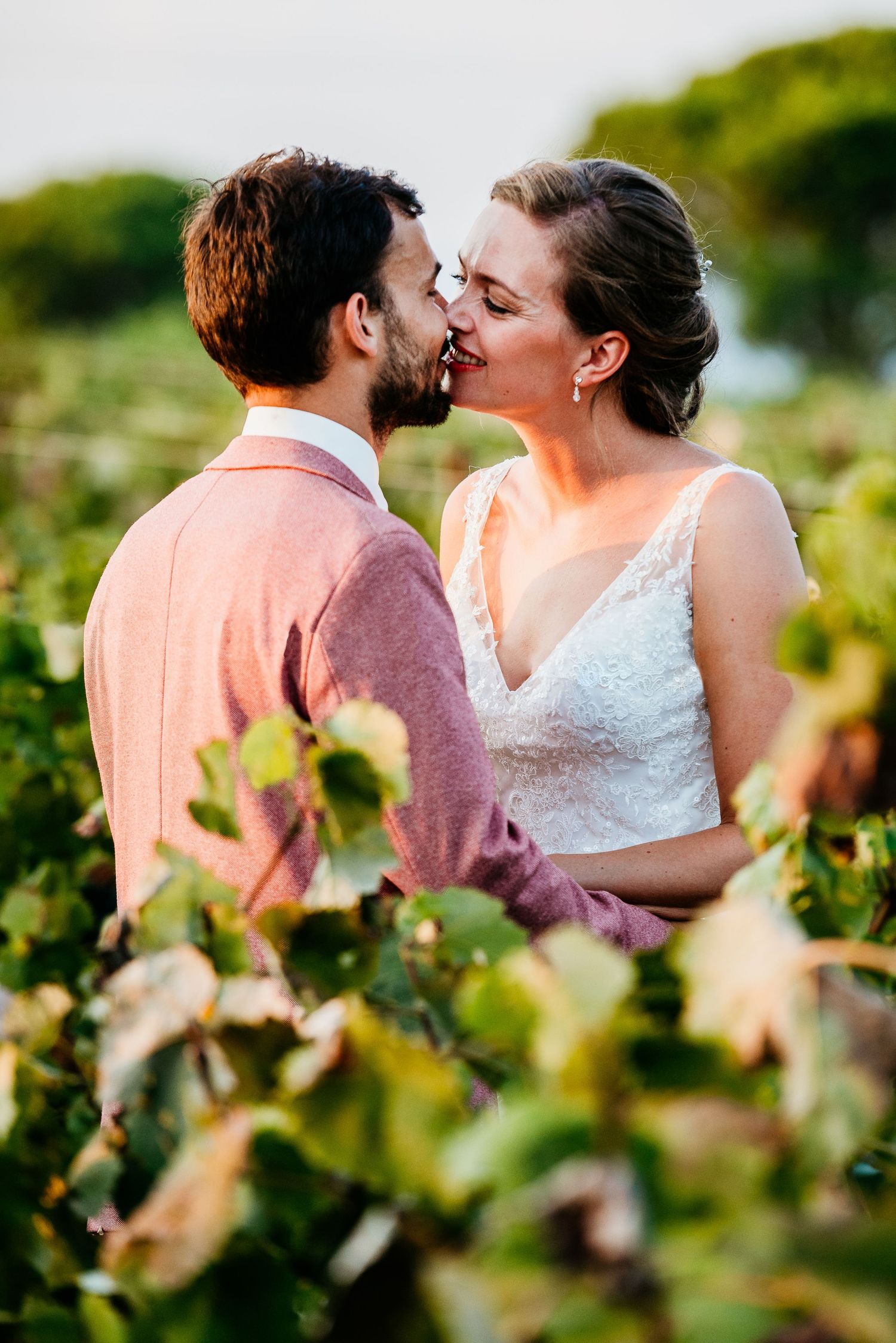 A romantic sunset moment shared between a couple in a vineyard wearing wedding attire.