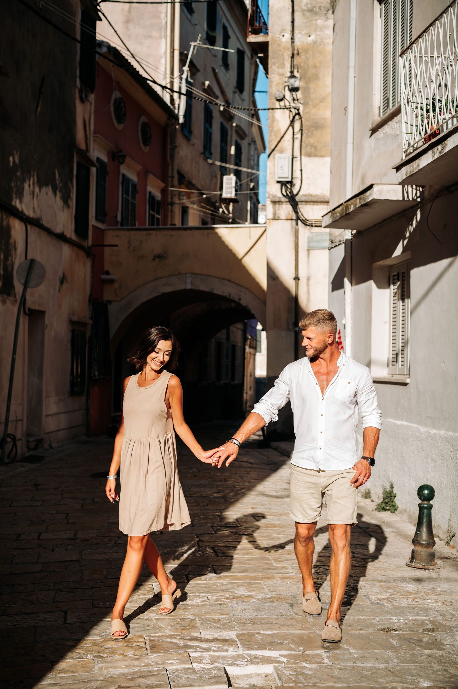 Playful couple dancing in narrow European alleyway with dramatic shadows.