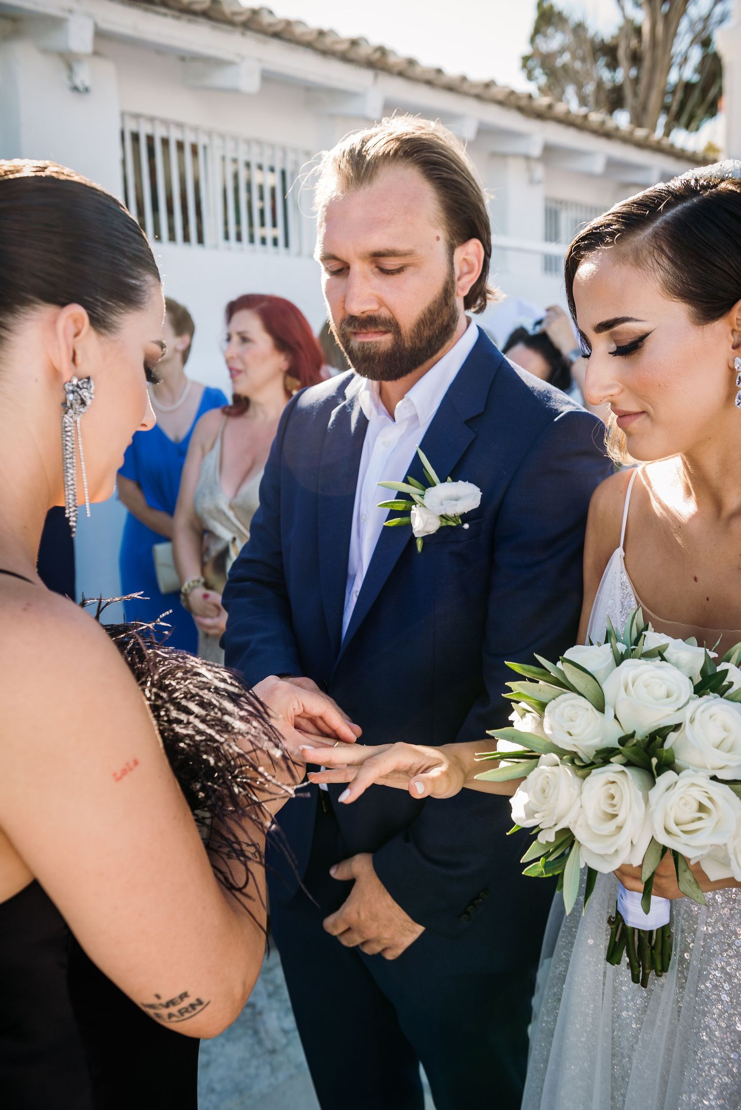 Wedding party members share an intimate moment with white rose bouquets outside a church.