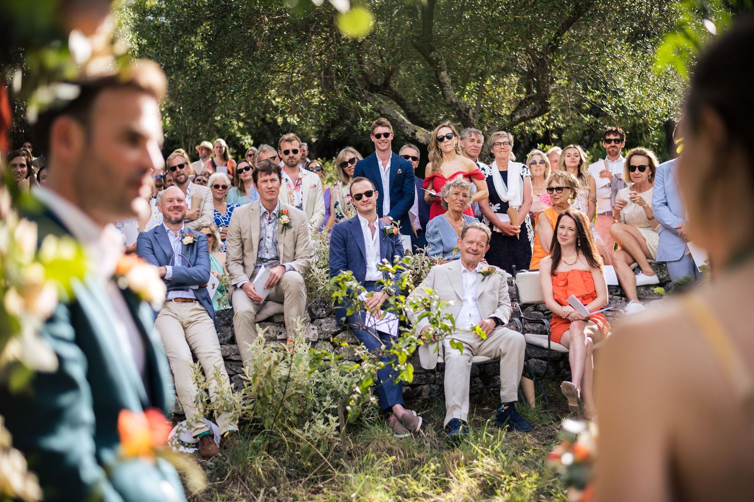 Large group of wedding attendees seated outdoors watching the ceremony.