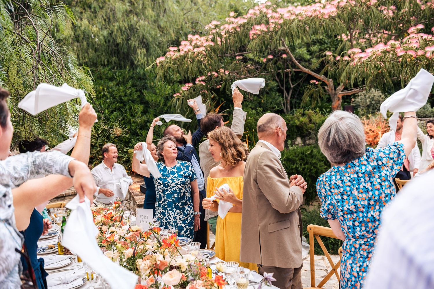 Wedding guests celebrate outdoors with raised arms against a natural garden backdrop.