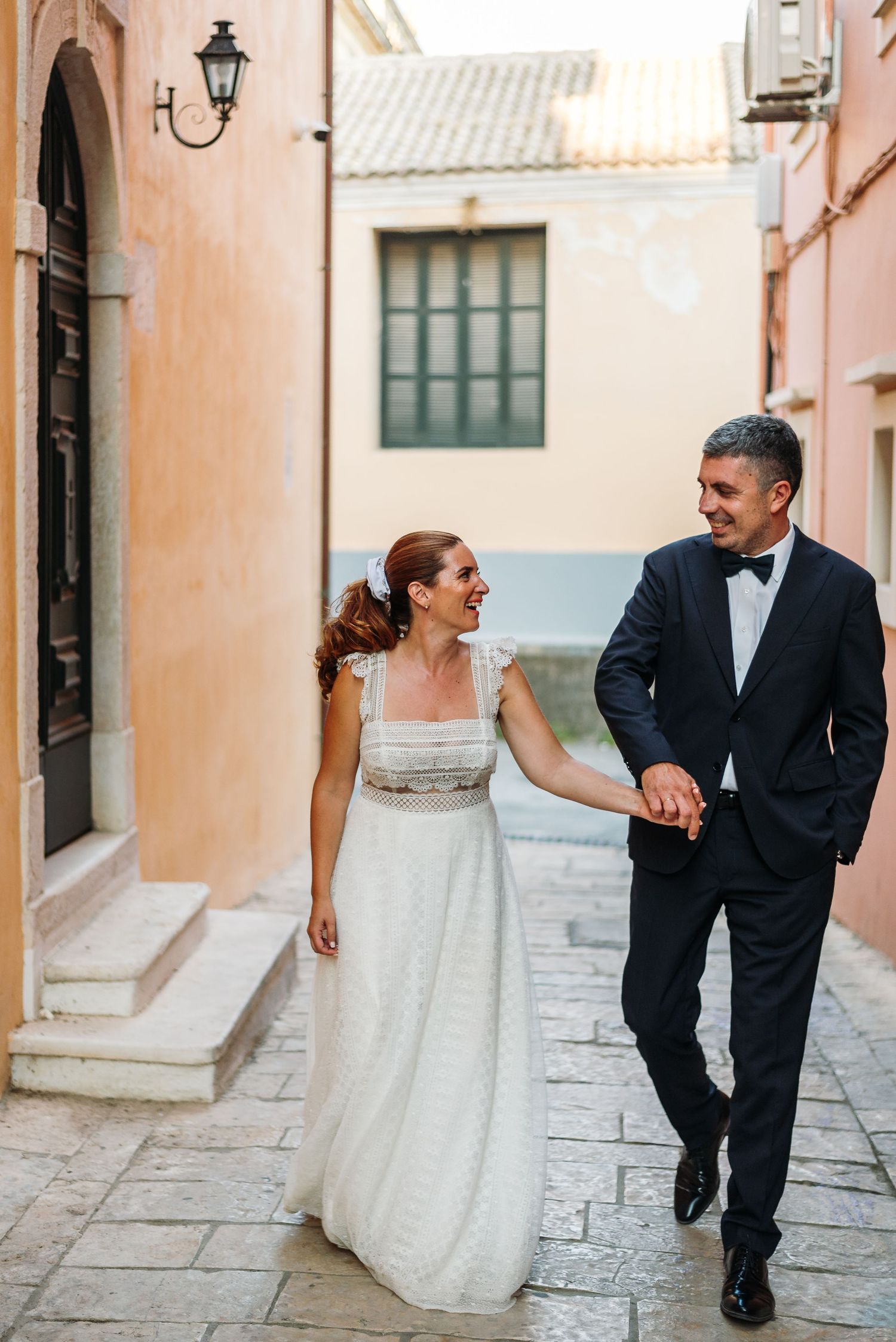 Playful wedding portraits on a quaint Mediterranean street with peach-colored walls.