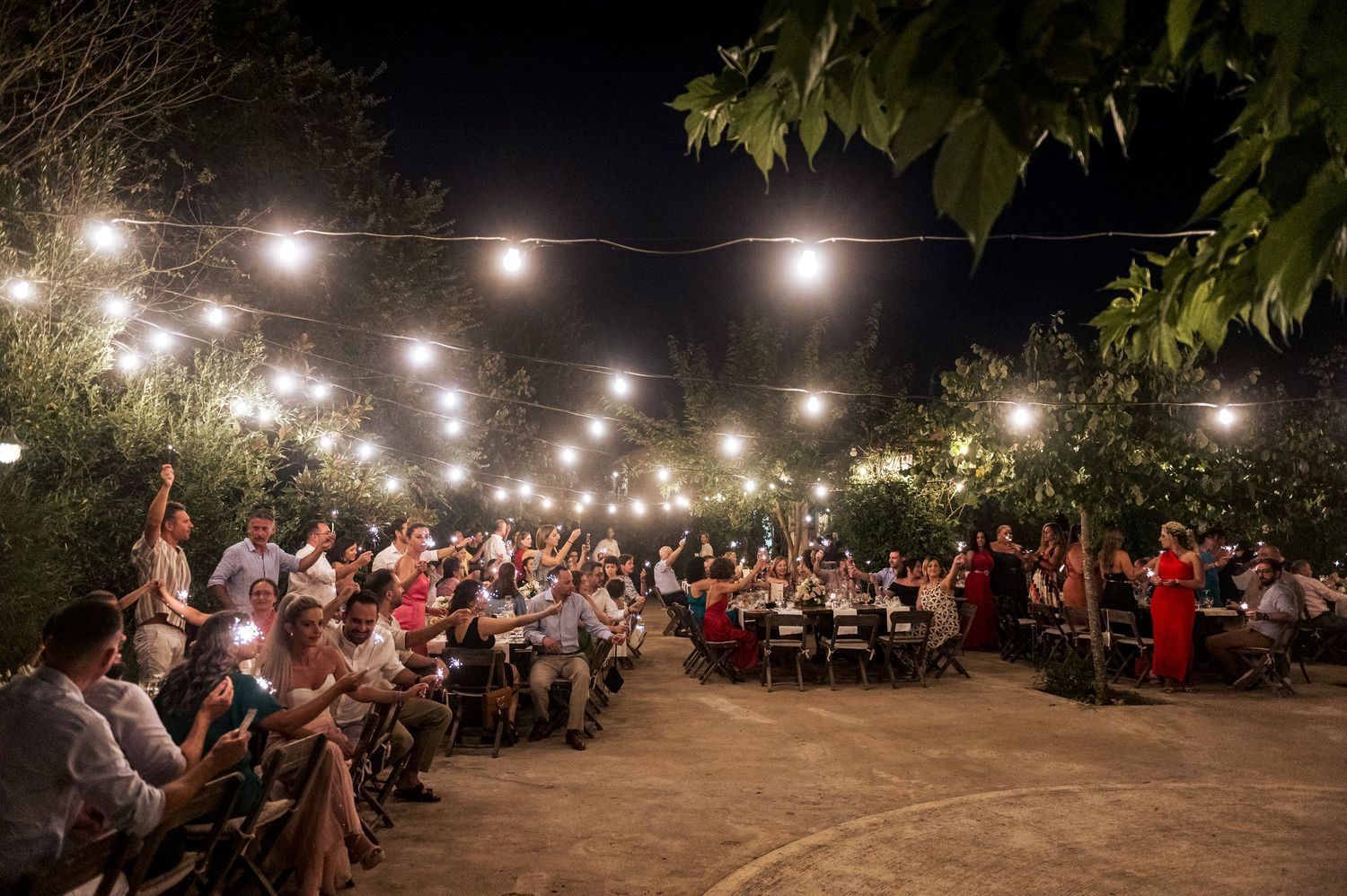 Wedding reception at night with string lights illuminating guests seated at long tables.