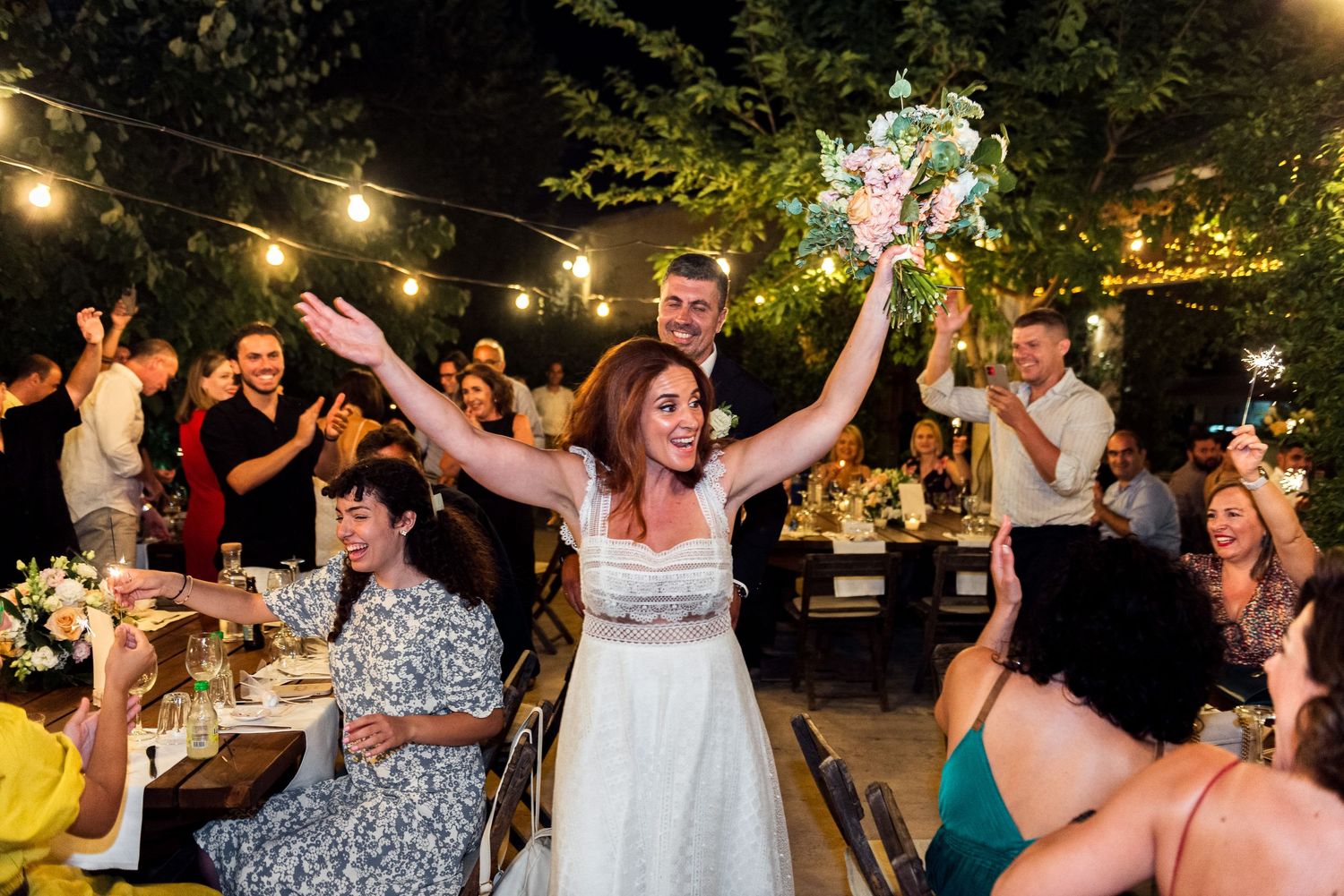 Wedding celebration with guests dancing and celebrating under outdoor string lights.