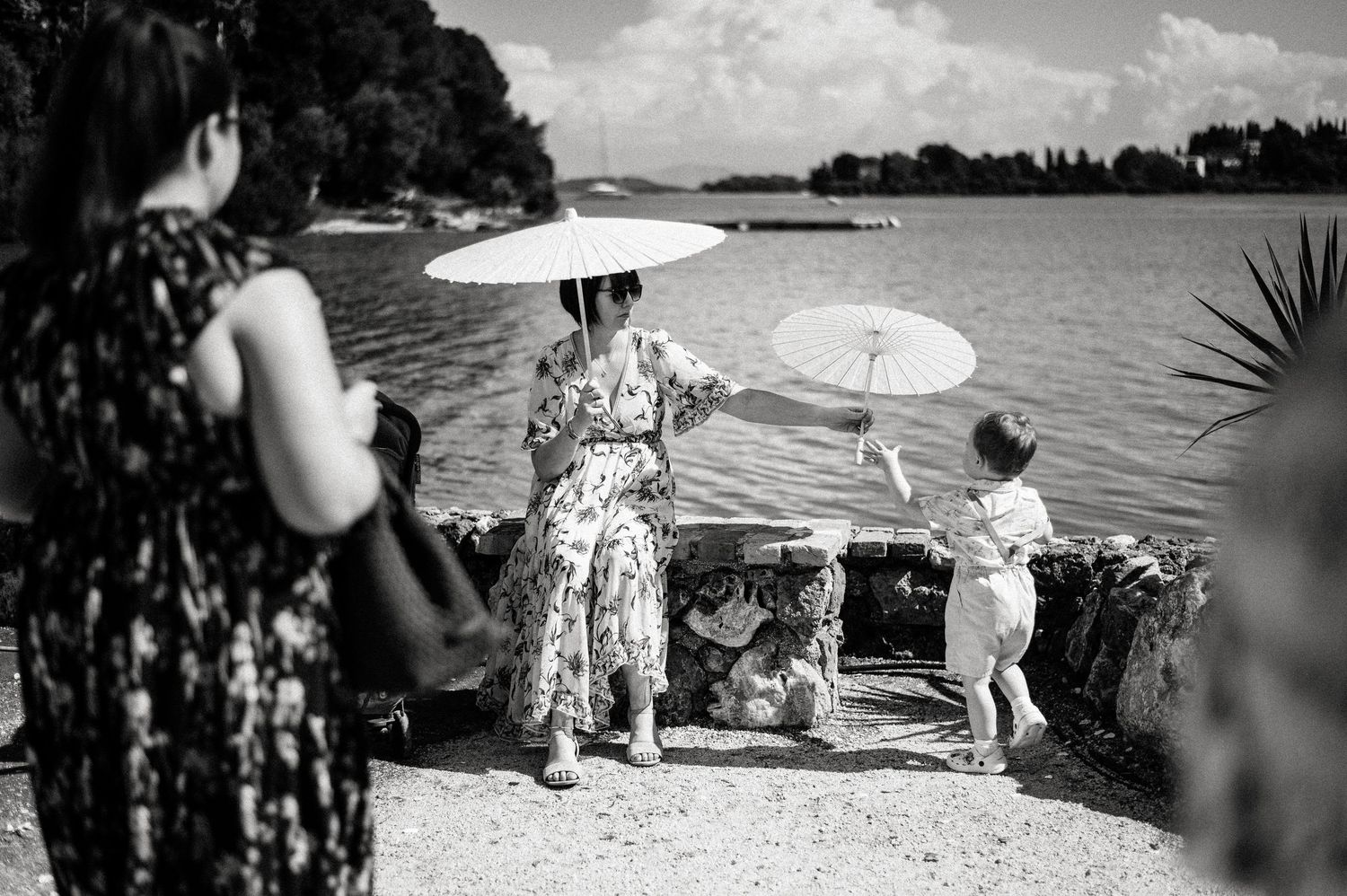 Wedding party walking along a scenic path holding white parasols on a sunny day.