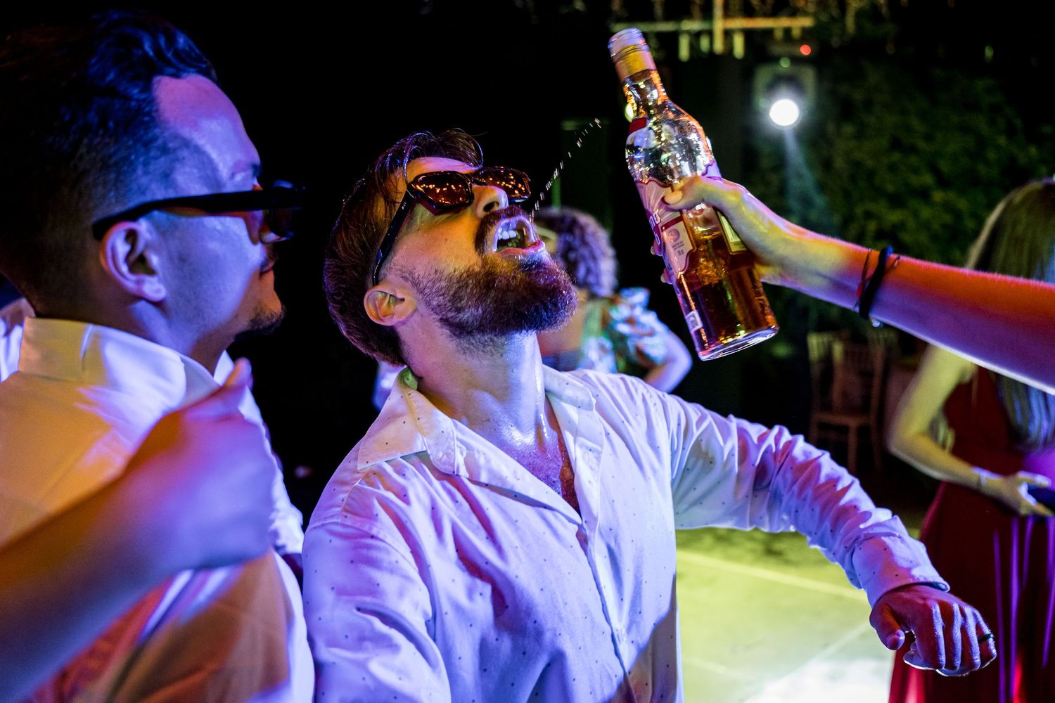 Dance party scene with guests in white shirts celebrating under nighttime lighting.