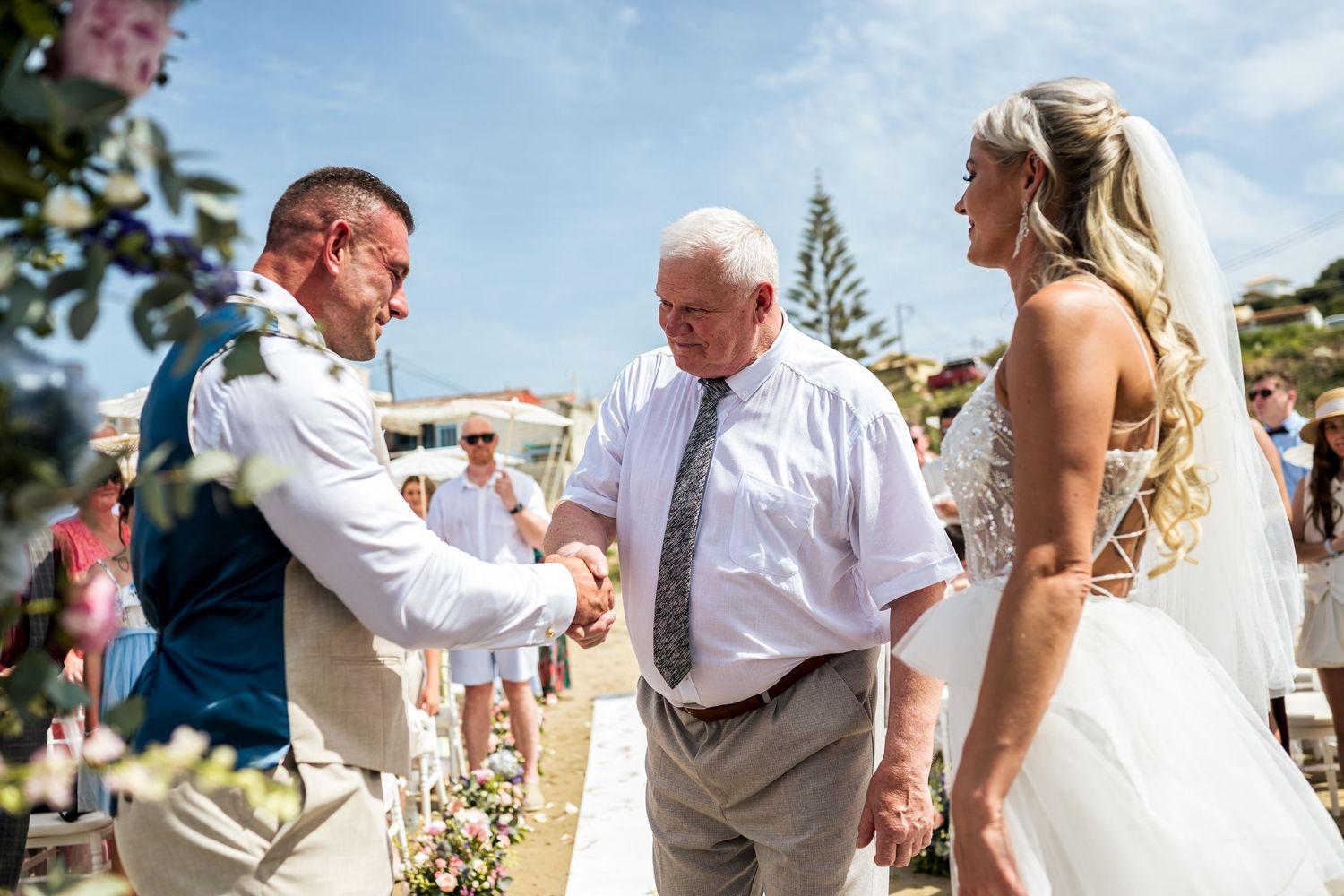 Guests mingle at outdoor beach wedding reception with blue skies.