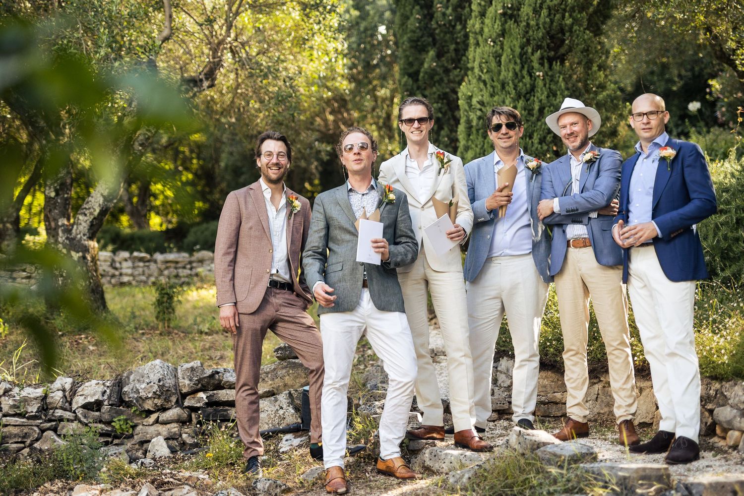 Group photo of wedding party members in coordinated beige and white outfits outdoors.