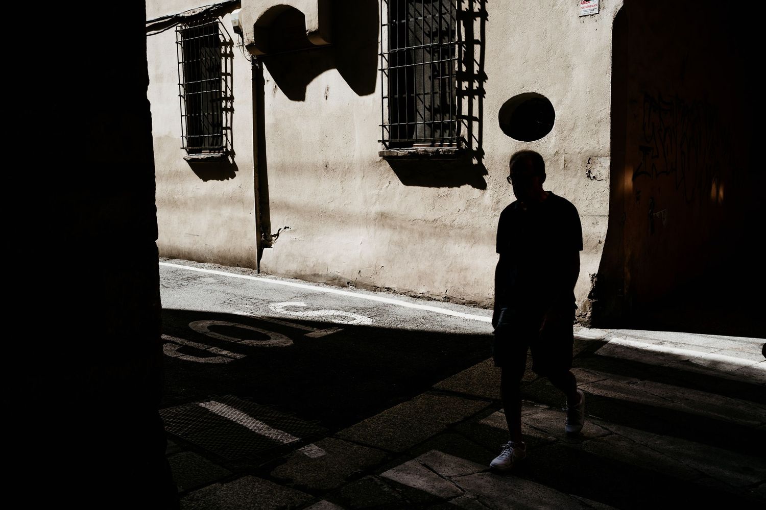 Dark silhouettes of people walking through an arcade corridor with dramatic lighting and shadows.