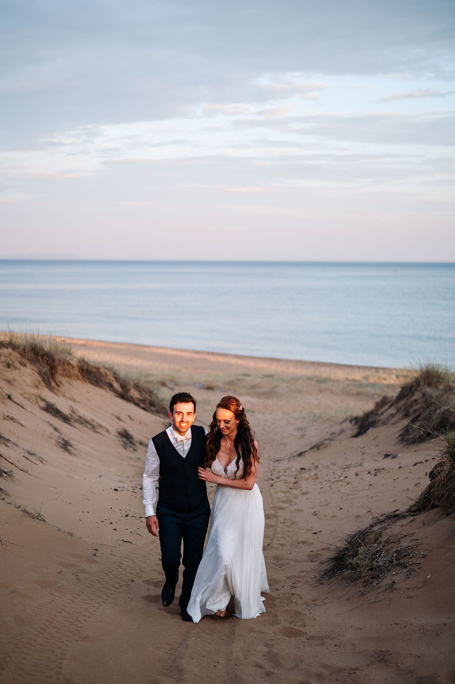 Couple walking along sandy beach dunes during sunset wedding photo session.