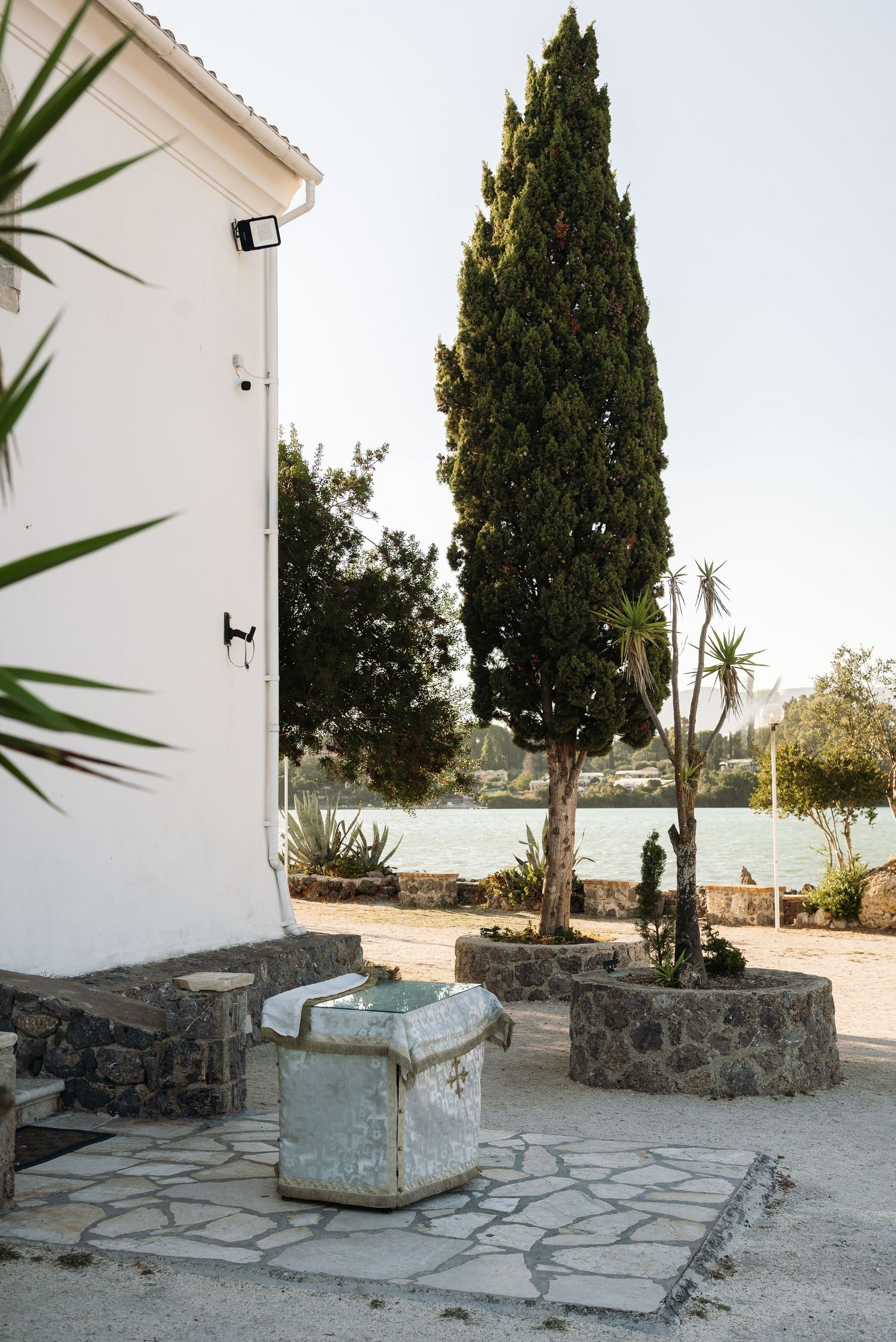 Stone benches and cypress trees line the exterior of a white Mediterranean church.