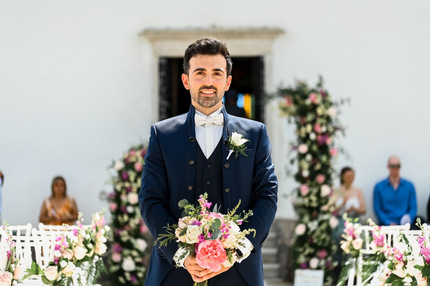 Elegant wedding ceremony setup with floral arrangements and white decor against a light backdrop.