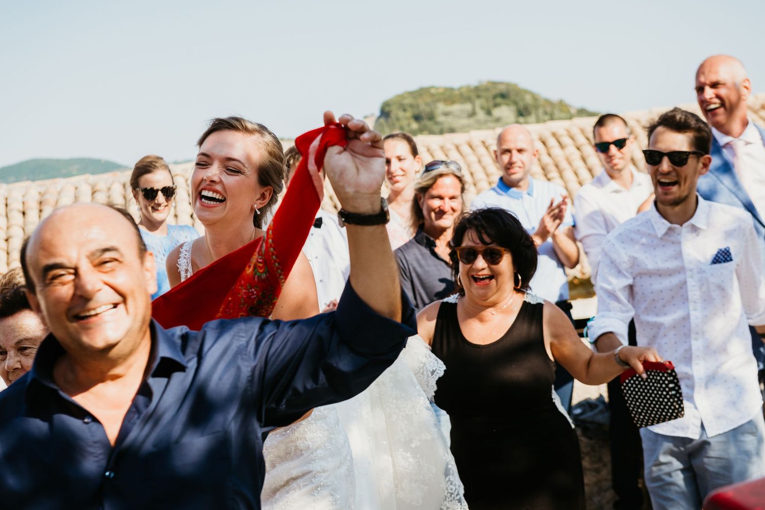 Wedding guests celebrate outdoors with enthusiastic expressions and raised hands.