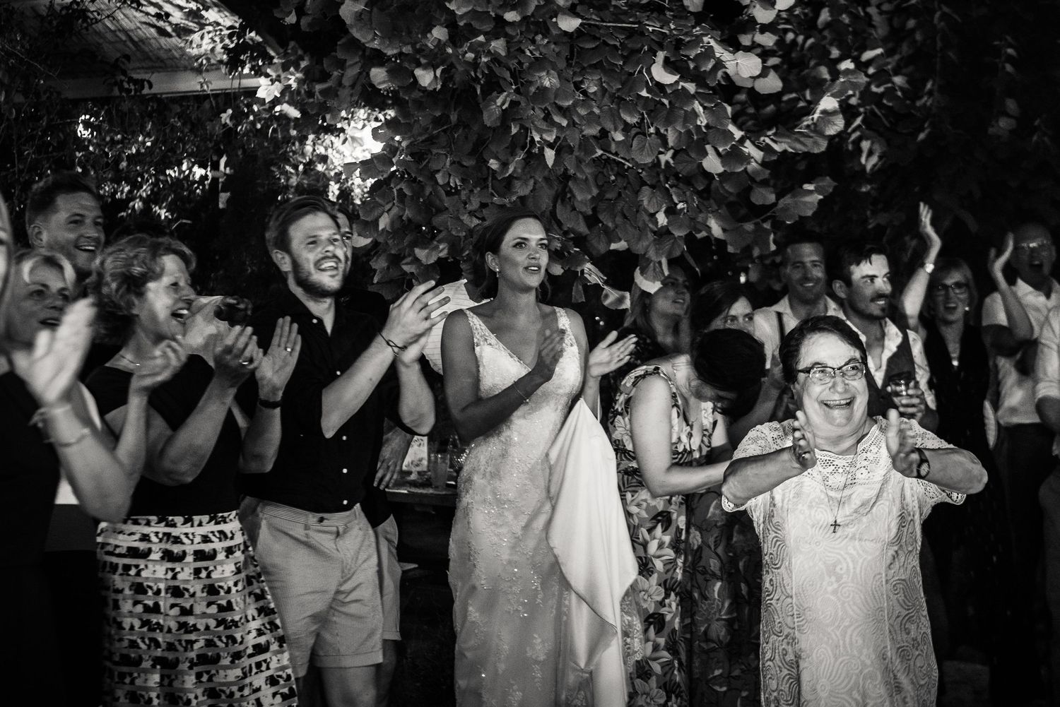 Black and white photo of wedding guests dancing and celebrating at an outdoor reception.