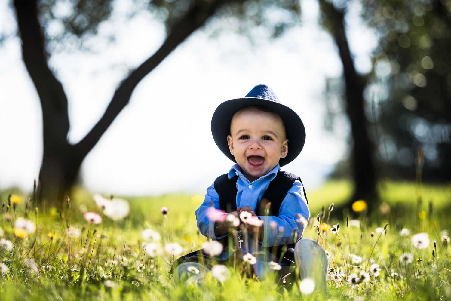 Young child laughs joyfully while playing in a field of dandelions on a sunny spring day.