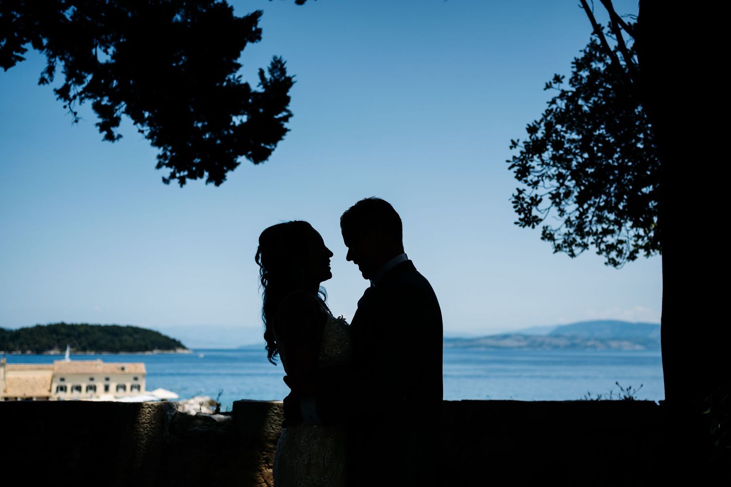 Silhouettes of a couple against a scenic ocean backdrop at sunset.
