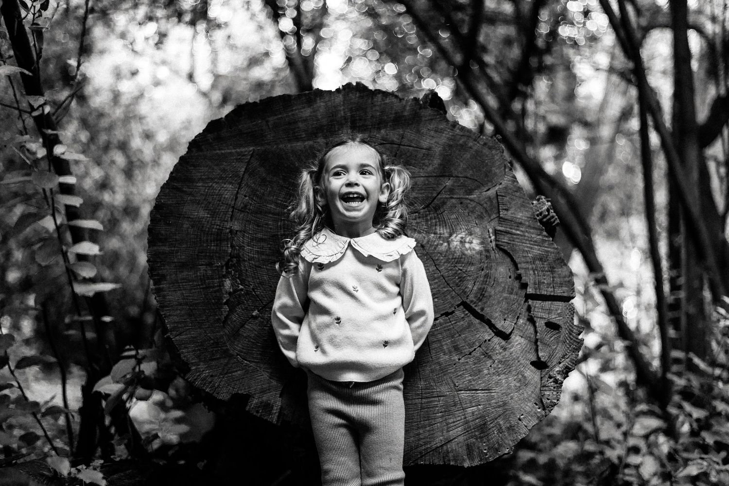 Black and white portraits of a child sitting against a rustic log backdrop.