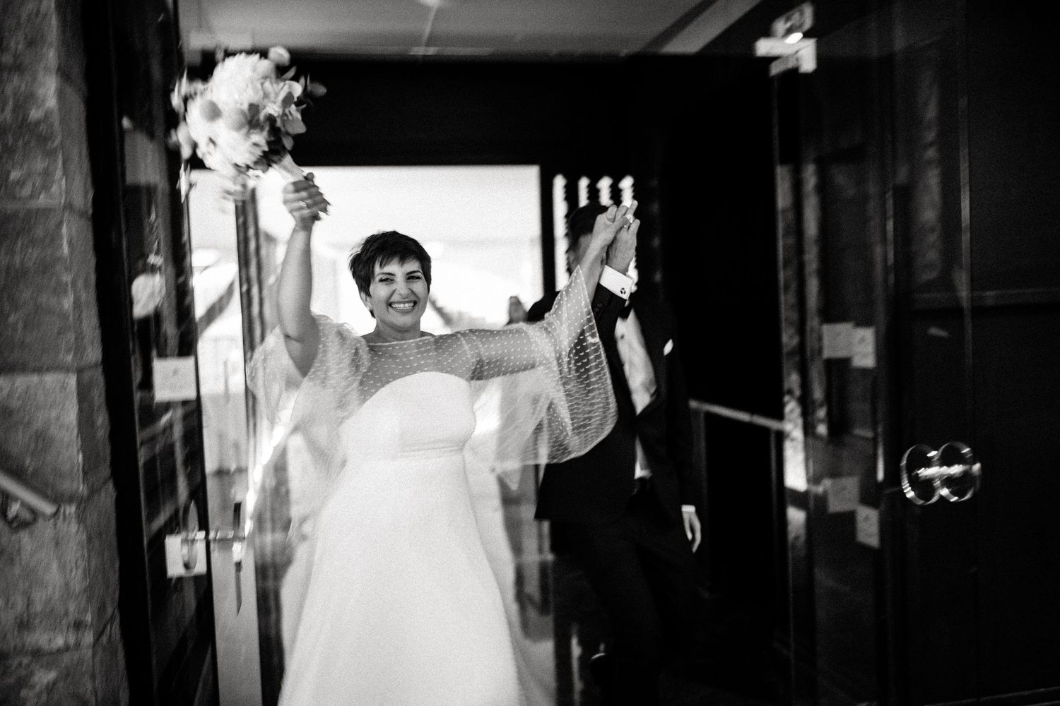 Black and white photo of wedding guests dancing and celebrating in a dimly lit venue.