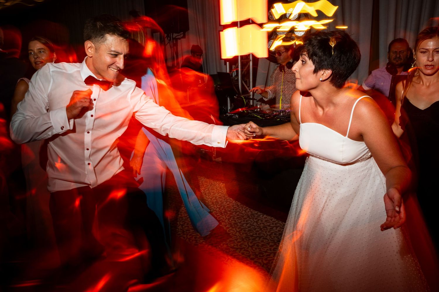 Wedding reception dancers illuminated by dramatic red lighting create dynamic party atmosphere.