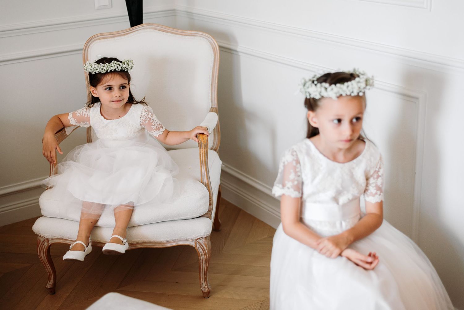Young attendants in white dresses and floral crowns sitting in elegant chairs.